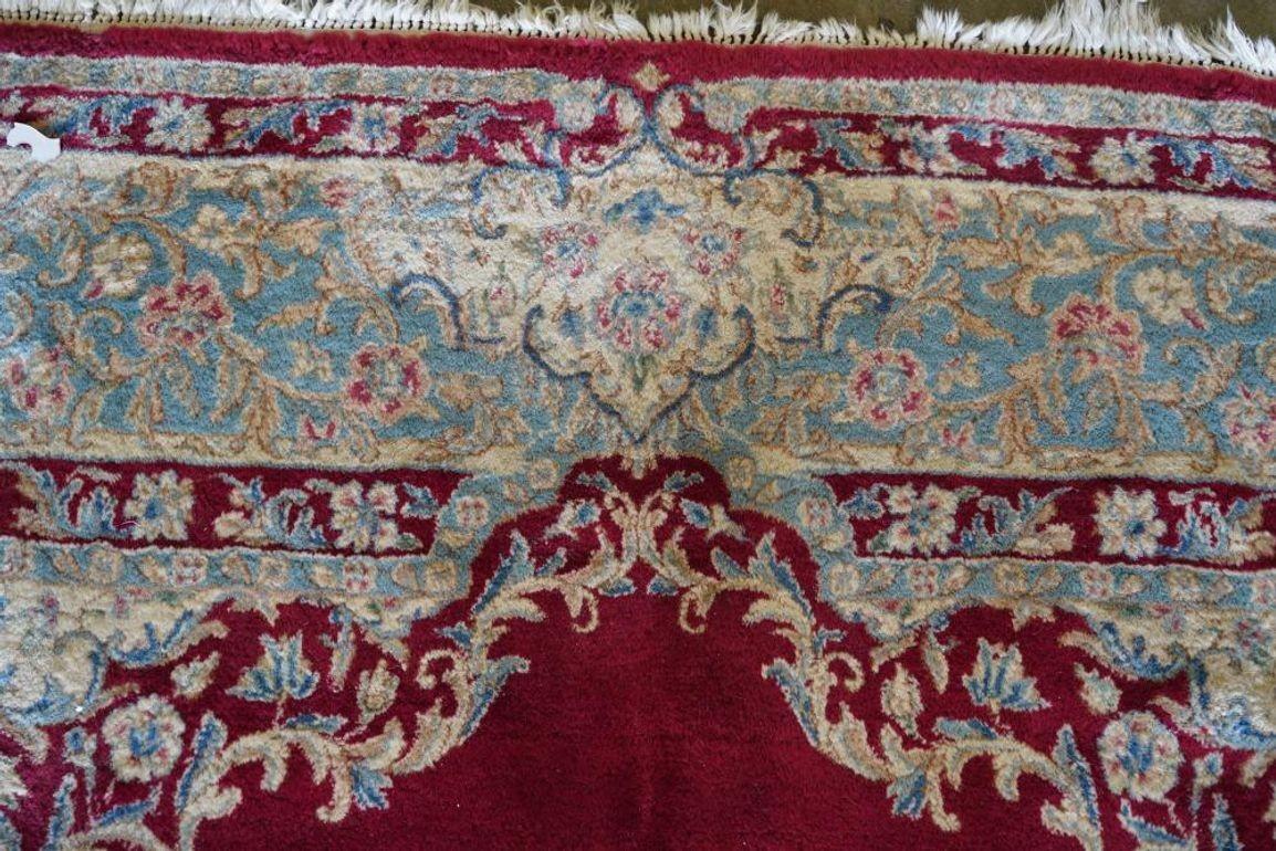 Exceptionnel tapis persan en laine et coton réalisé au début du 20e siècle, présentant un magnifique décor rouge et des tons pastel (bleu, crème, rose). Il est orné de motifs traditionnels et de dessins botaniques sur tout le pourtour de la