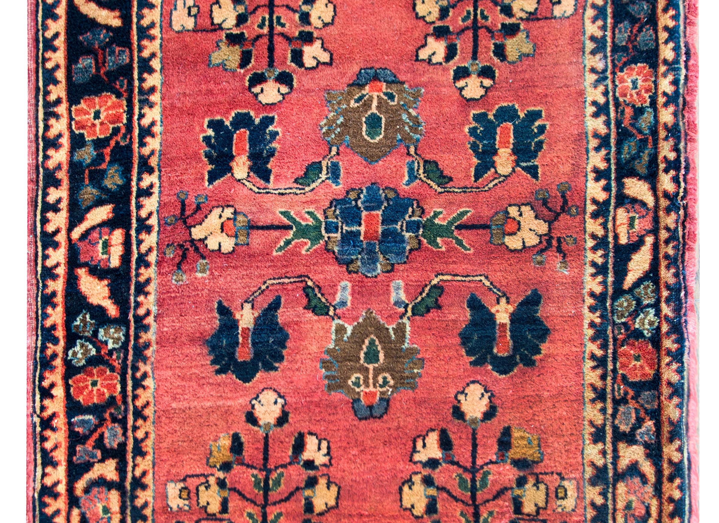 A sweet early 20th century Persian Sarouk rug with a simple but beautiful mirrored floral pattern woven in indigo, brown, green, ream, and pink, set against a pink background, and surrounded by a wonderful stylized floral border flanked by more