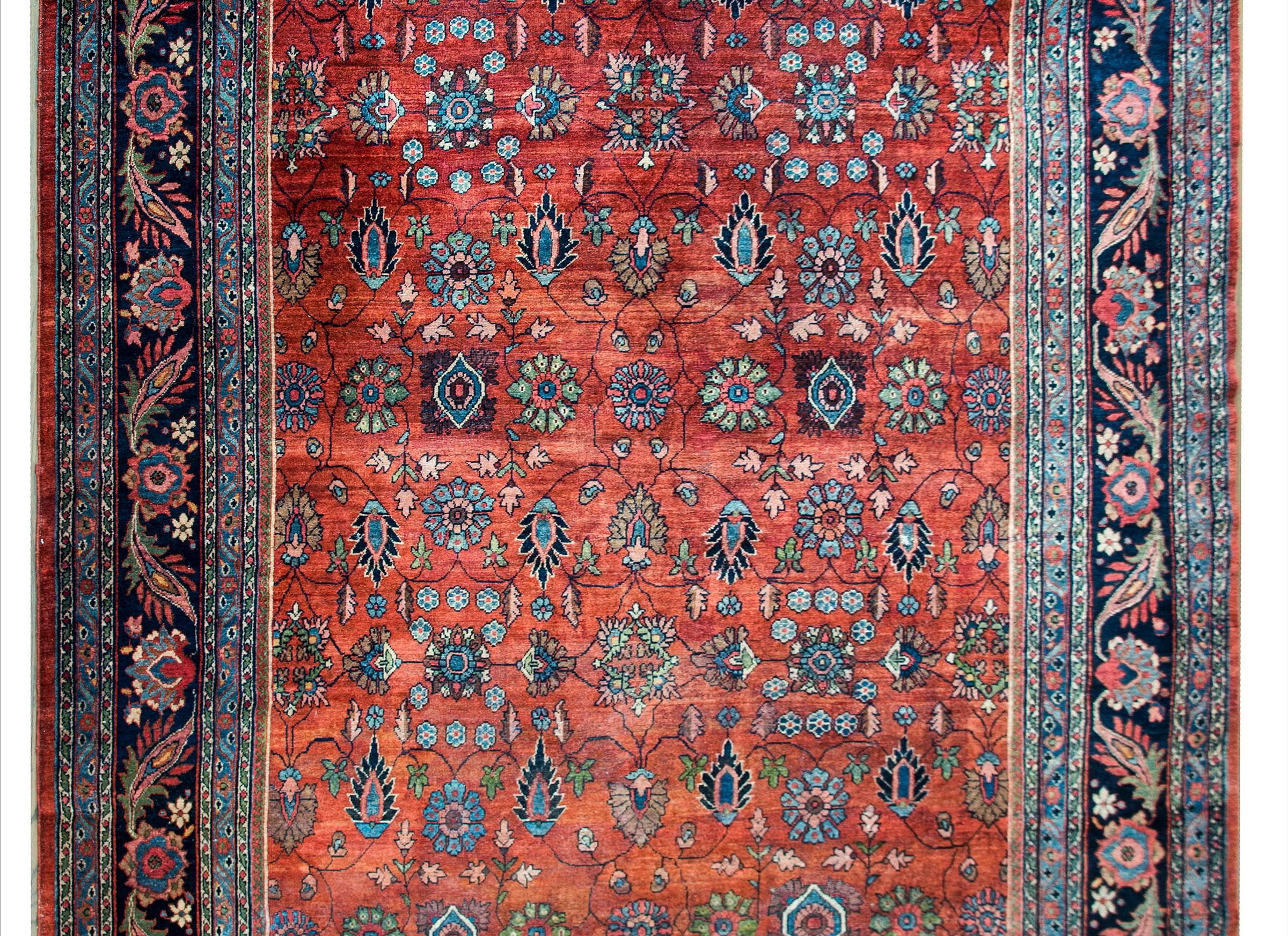 A beautiful early 20th century Persian Sarouk Mahal rug with an all-over floral pattern with myriad flowers and thin scrolling vines woven in indigo, brown, cream, and pink, and set against a crimson background. The border is complex with a wide