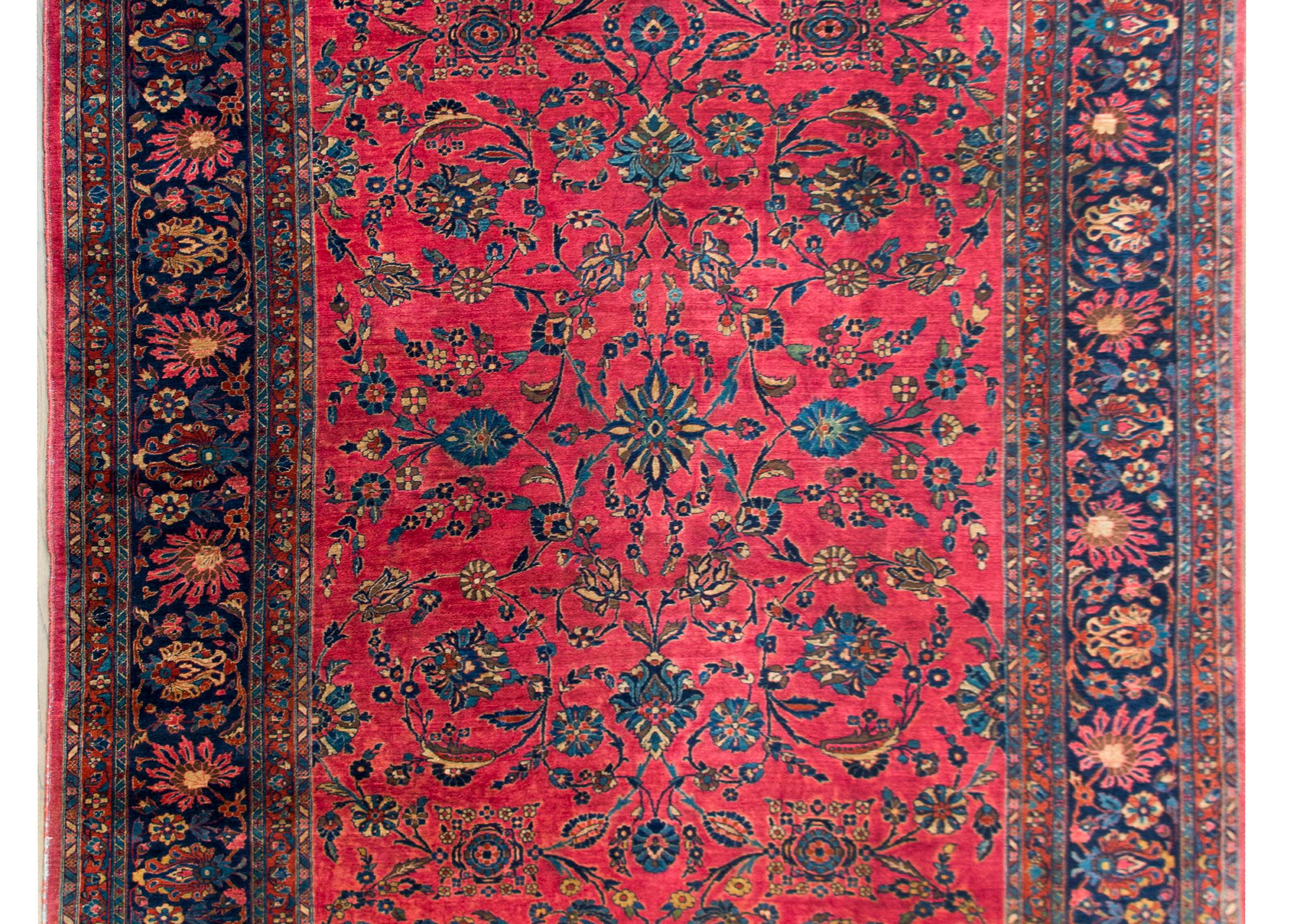 An incredible large-scale early 20th century Persian Sarouk Mahal rug with a mirrored floral and scrolling vine pattern woven in light and dark indigo, cream, and pink, set against a brilliant cranberry field, and surrounded by a wide border with
