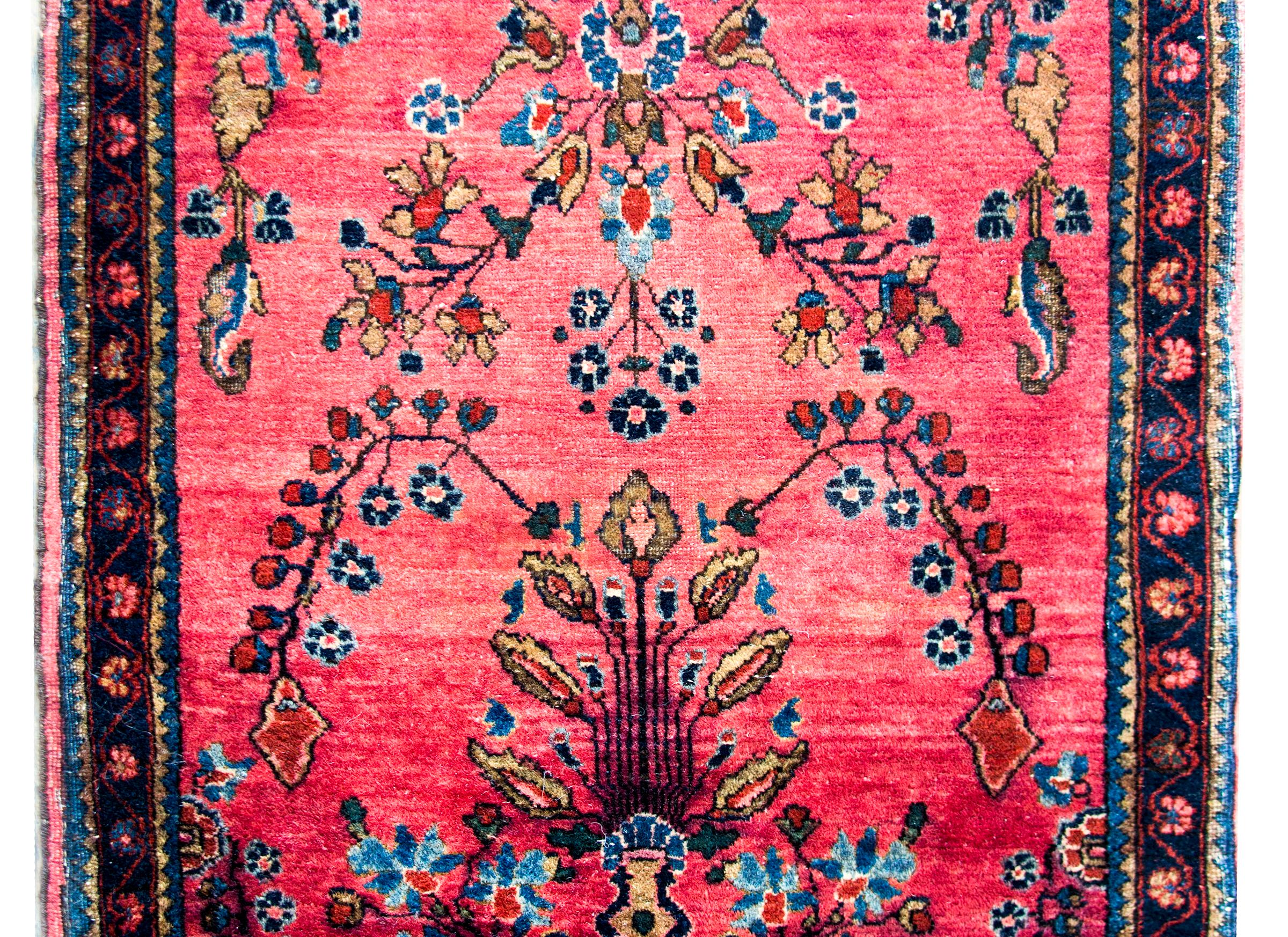 A stunning early 20th century Persian Sarouk Mohajeran rug with a mirrored floral and vine pattern woven in pink, light and dark indigo, and cream, set against a cranberry background, and surrounded by a simple border composed of multiple petite
