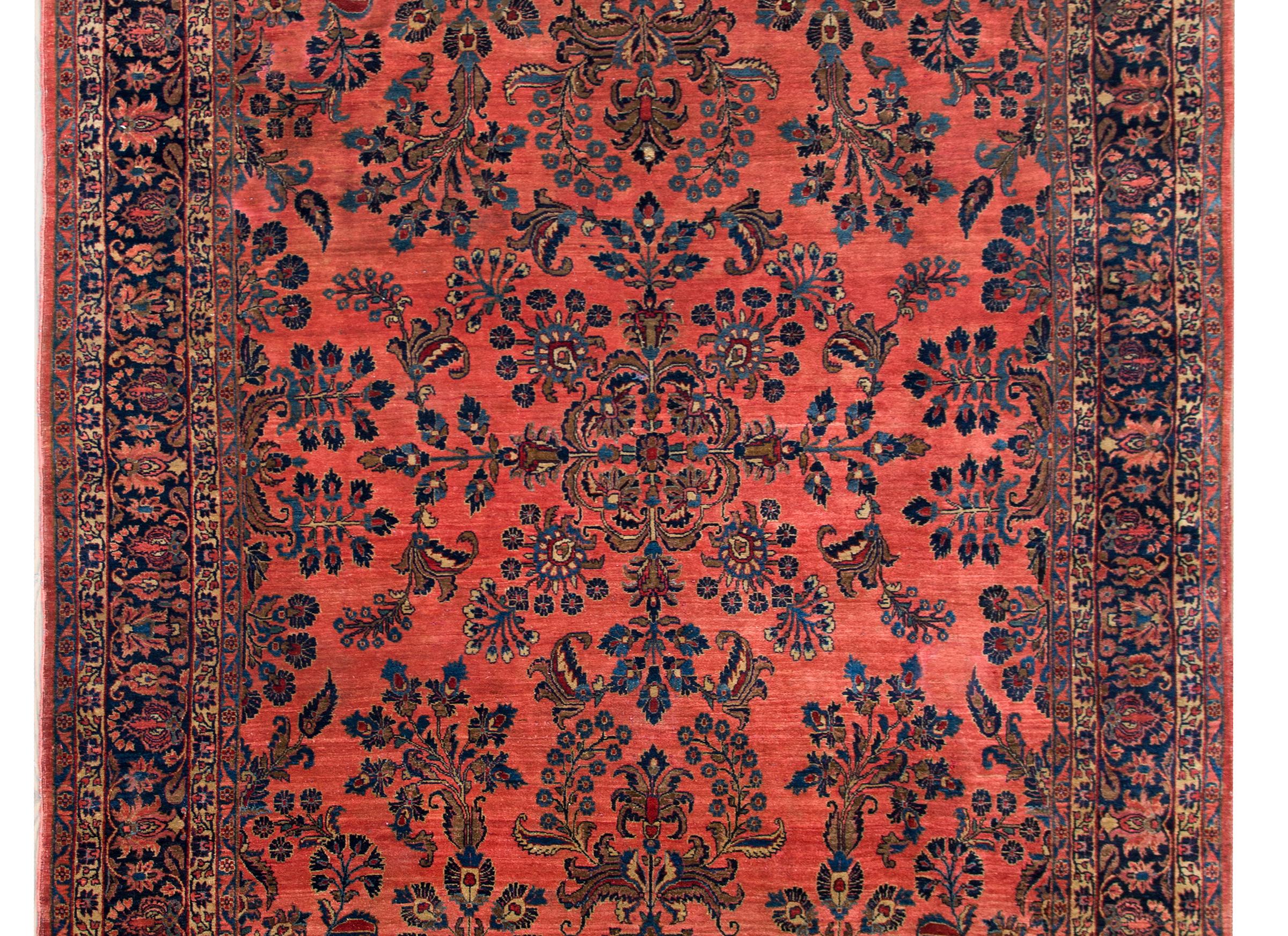 A gorgeous early 20th century Persian Sarouk Mohajeran rug with a mirrored floral pattern with beautifully rendered flowers and scrolling vines all woven in light and dark indigo, cranberry, and cream, set against a salmon colored background, and
