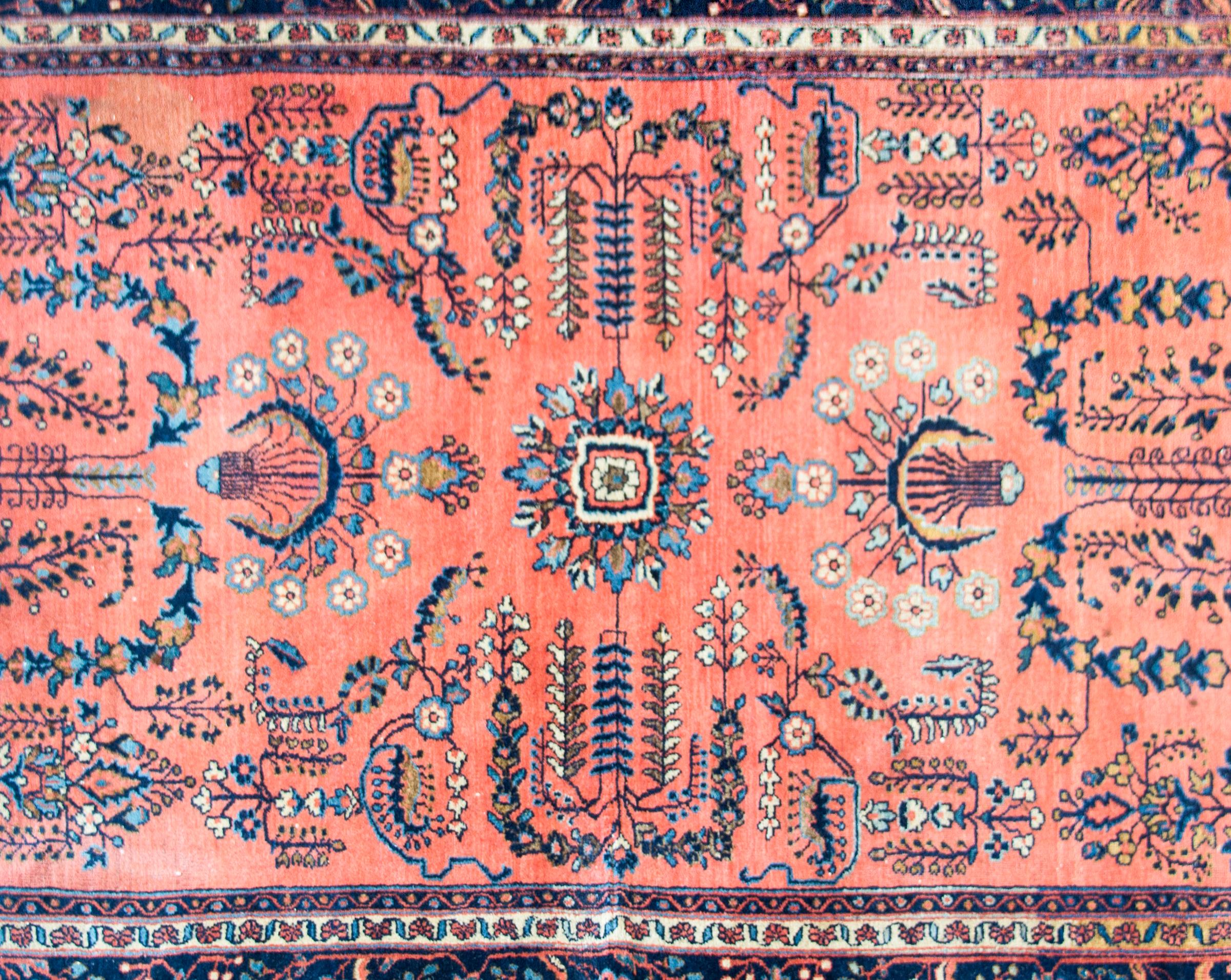 A beautiful early 20th century Persian Sarouk Mohajeran rug with a mirrored floral pattern woven in light and dark indigo, cream, and pink, set against a salmon colored background and surrounded by a wide floral and leaf patterned stripe border