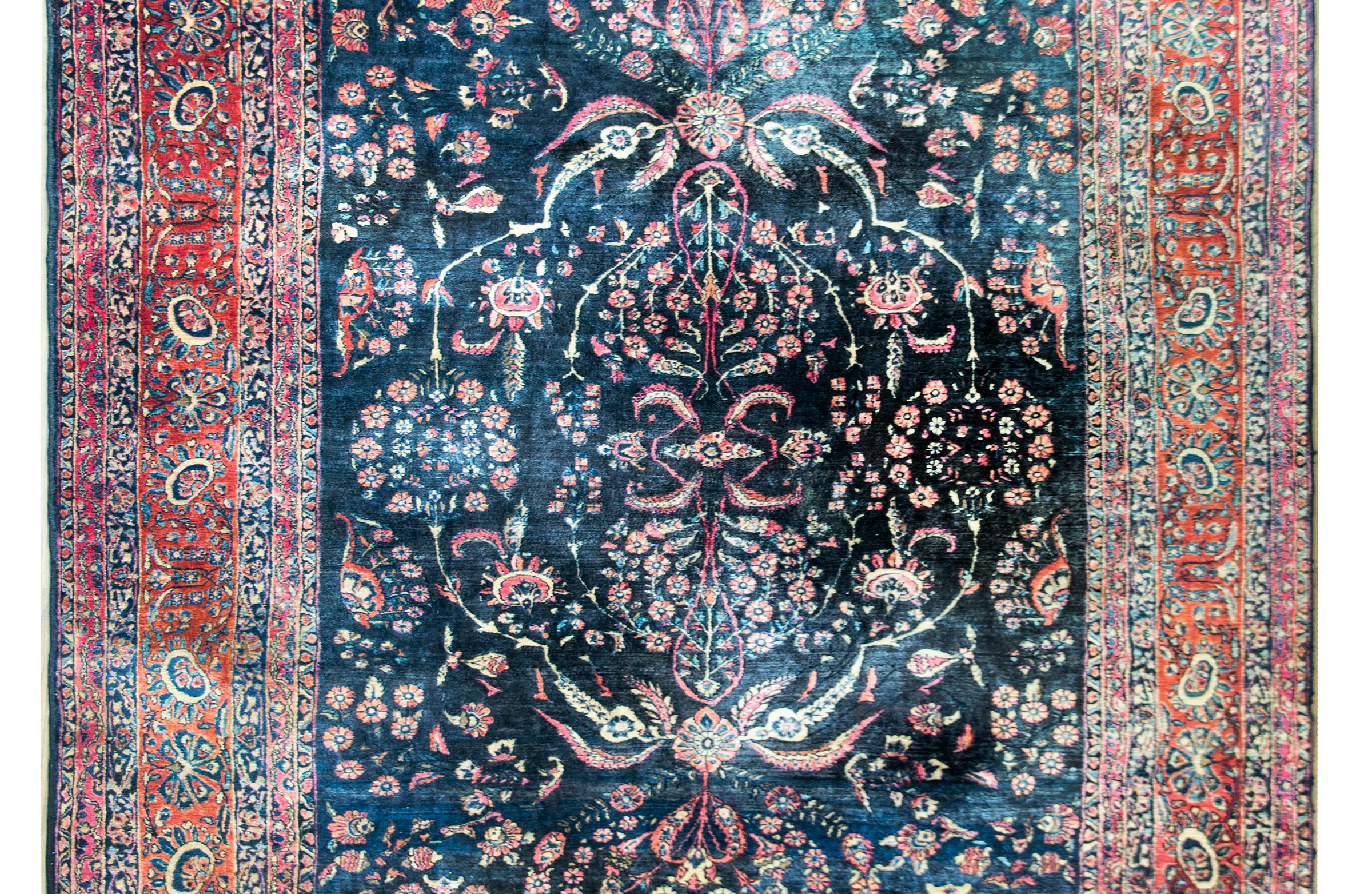 A beautiful large early 20th century Persian Sarouk Mohajeran rug with a lacy mirrored floral pattern in the center woven in traditional Sarouk colors of pink, crimson, creams and indigo, and set against a dark indigo background. The border is