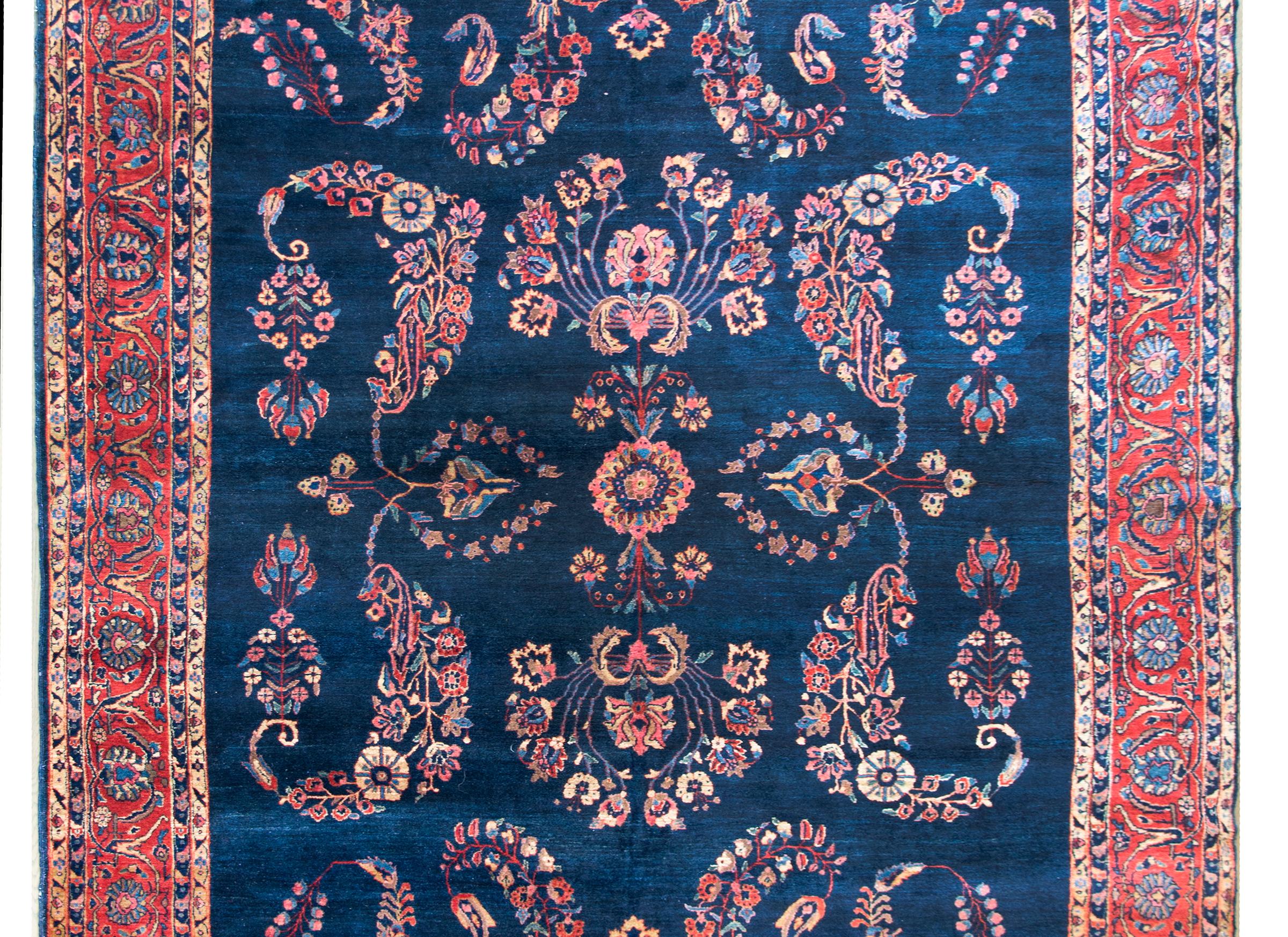 A wonderful early 20th century Persian Sarouk Mohajeran rug with a large-scale mirror floral pattern woven in traditional Farouk colors including crimson, pink, cream, and light and dark indigo, and surrounded by a wide floral patterned border
