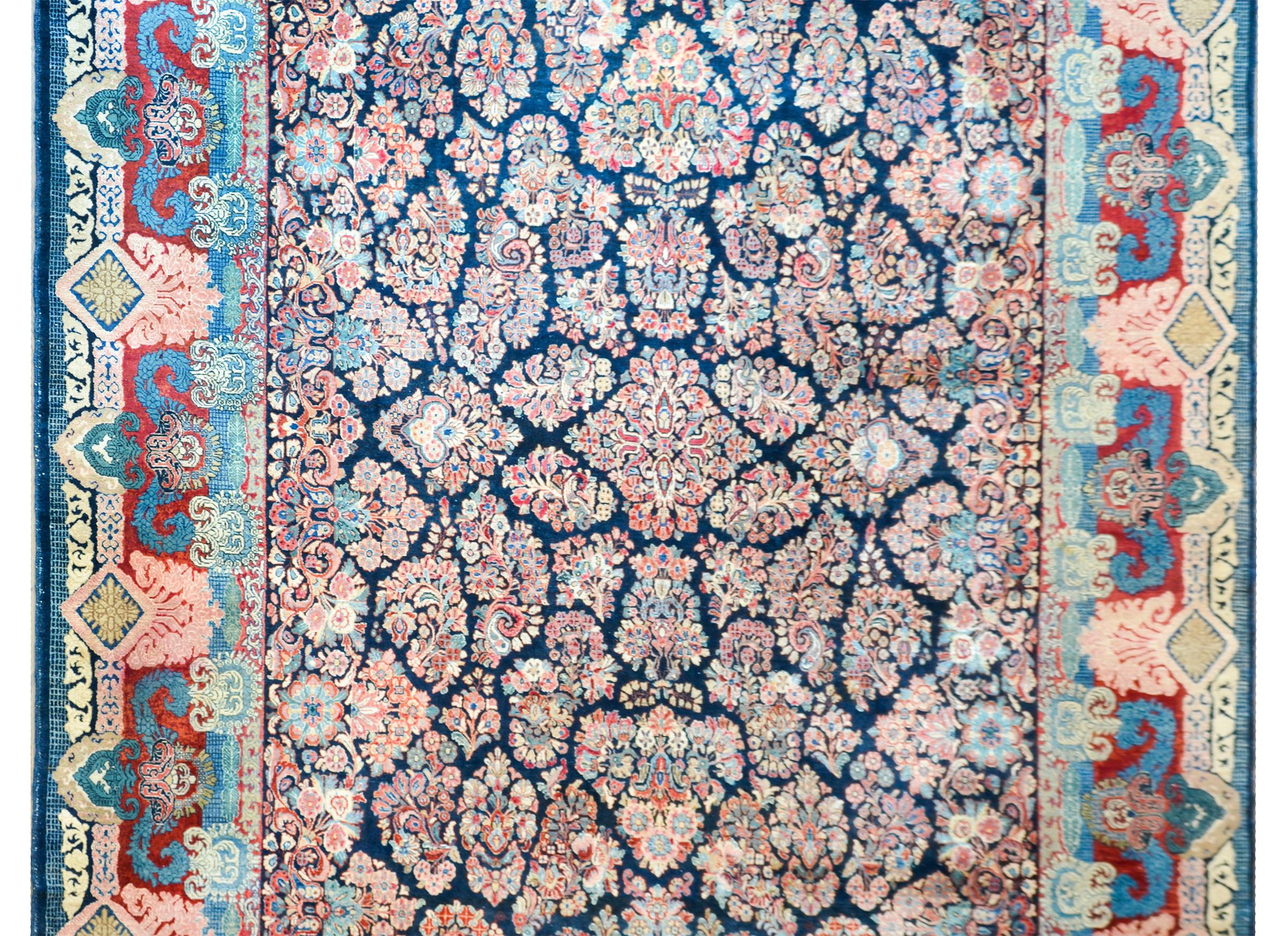 A striking early 20th century Persian Sarouk rug with an unusual mirrored floral cluster pattern woven in traditional pinks, indigos, creams, and cranberries, against a dark indigo background. The border is wide with multiple large-scale floral