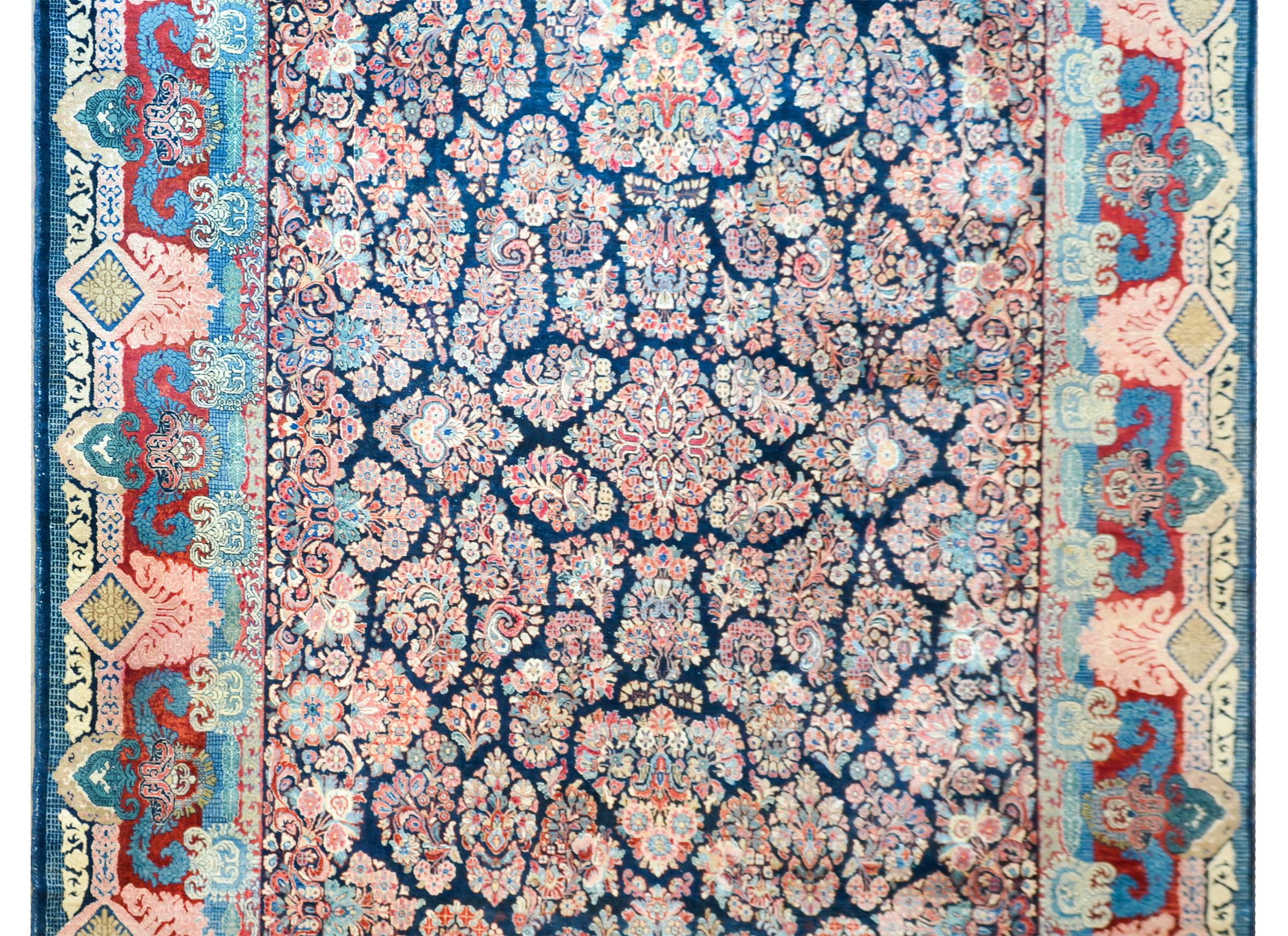 Sorprendente alfombra persa Sarouk de principios del siglo XX, con un inusual motivo de racimos florales espejados tejidos en los tradicionales rosas, índigos, cremas y arándanos, sobre un fondo añil oscuro. El borde es ancho con múltiples motivos