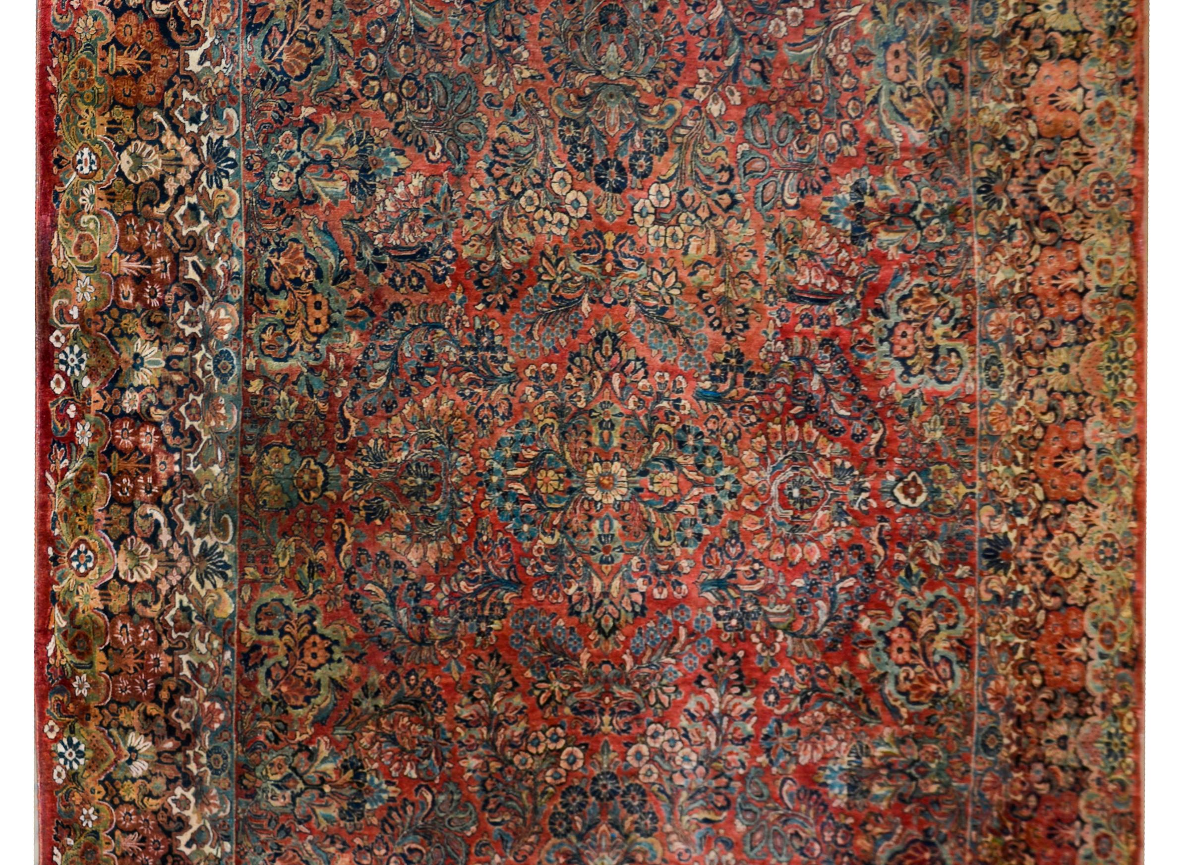 An incredible early 20th century Persian Sarouk rug with an incredible all-over floral cluster pattern woven in rich and dark colors including reds, creams, pinks, and light and dark indigos, all set against a dark cranberry background. The border