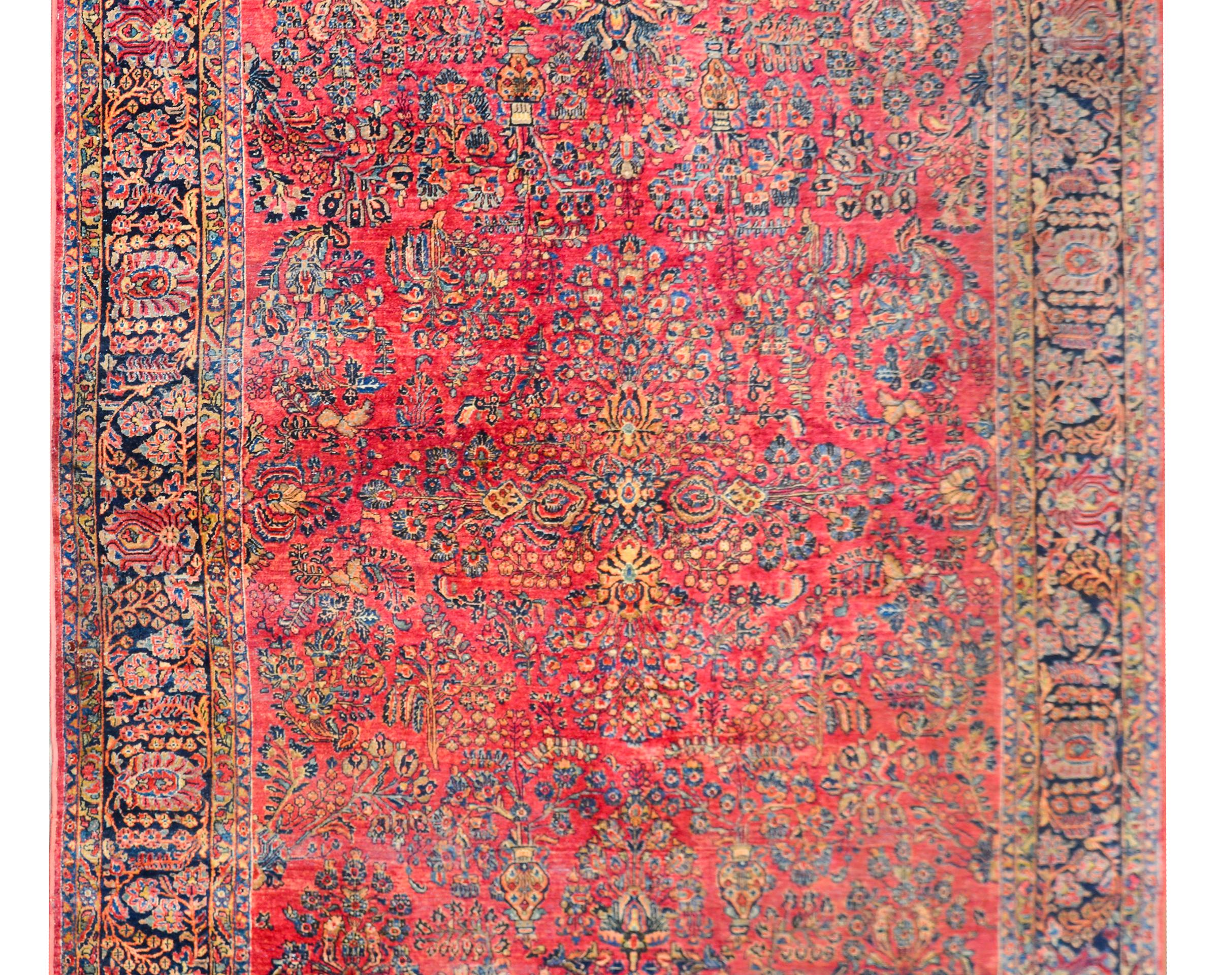 A wonderful early 20th century Persian Sarouk rug with a traditional mirrored floral cluster pattern woven in crimsons, pinks, light and dark indigos, and creams, set against a cranberry colored background, and surrounded by a wonderful wide floral