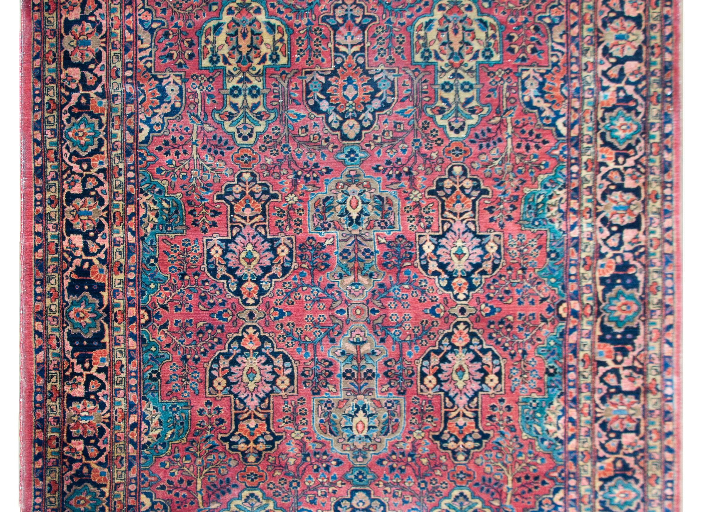 A fantastic early 20th century Persian Sarouk rug with a beautiful mirrored floral patterned field with large stylized floral shapes amidst a densely woven field of trees-of-life and other flowers, all woven in beautiful indigos, pinks, creams, and
