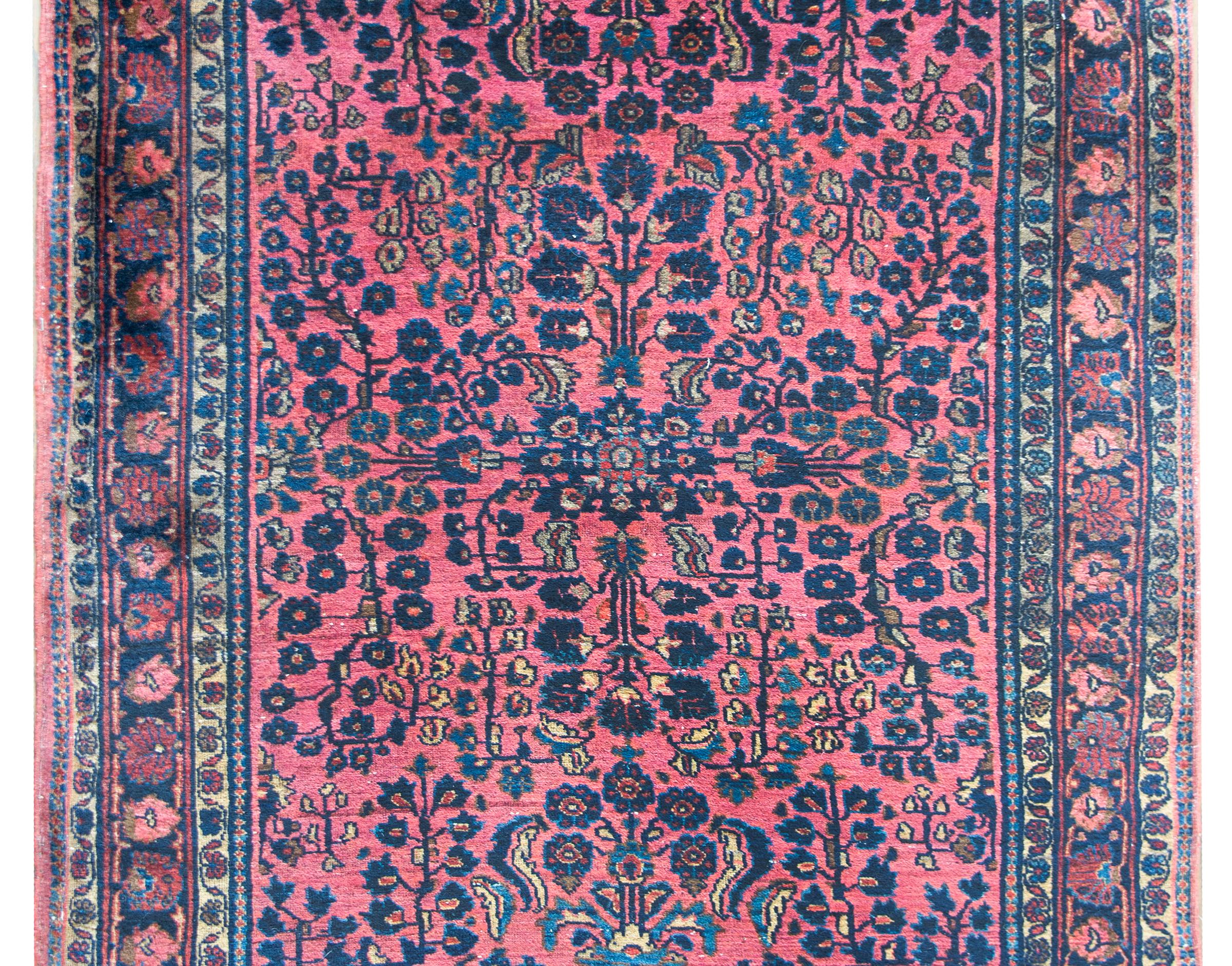 A beautiful early 20th century Persian Sarouk rug with a mirrored pattern with scrolling vines and flowers woven in pink, cream, and light and dark indigo against a coral colored background.  The border is complex with myriad petite floral patterned