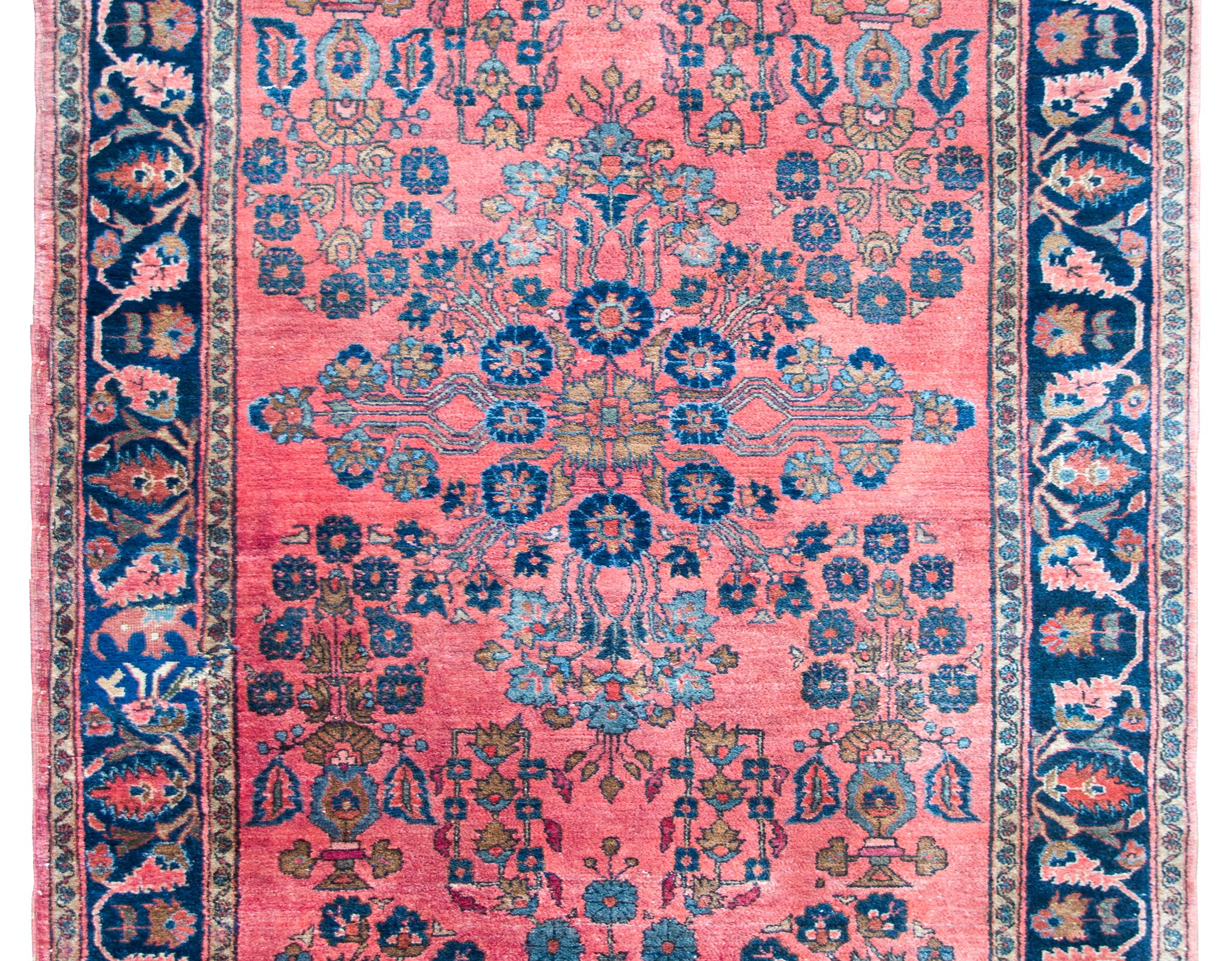A wonderful early 20th century Persian Sarouk rug with a central floral medallion amidst a field with a mirrored floral pattern all woven in pink, cream, and light and dark indigo, and set against a coral colored background. The border is beautiful