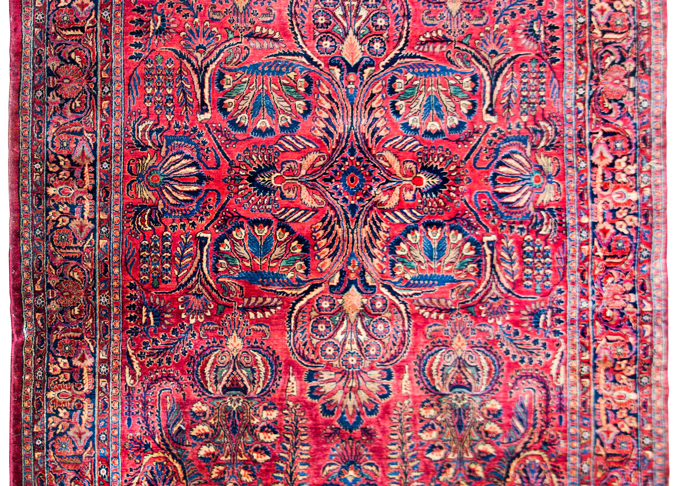 A stunning and rare early 20th century Persian Sarouk rug with the most incredible large-scale mirrored floral pattern containing myriad floral clusters that mimic peacock tails, all woven in light and dark indigo, pink, white, green, and yellow set