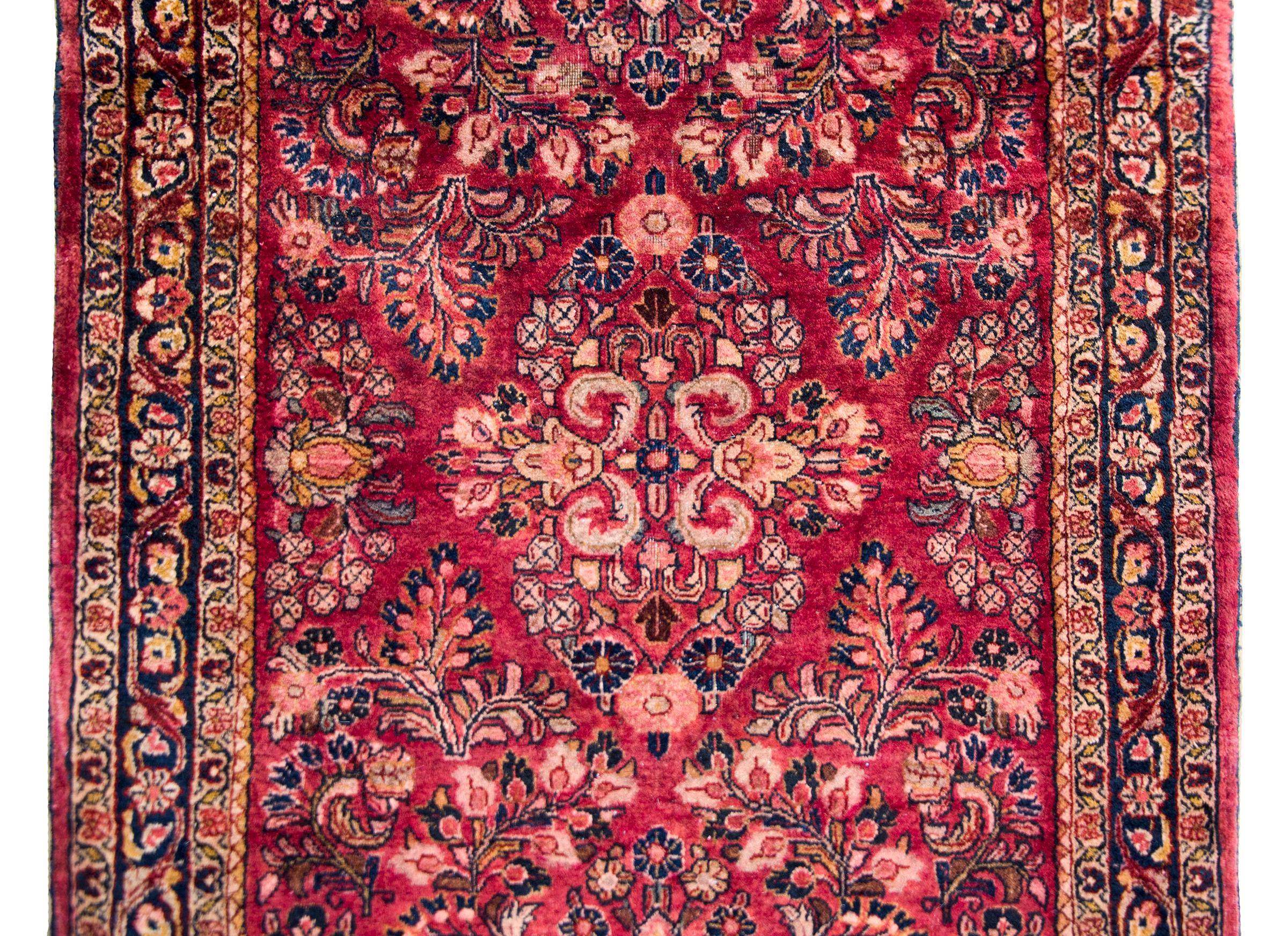 A remarkable early 20th century Persian Sarouk rug with a mirrored all-over floral cluster pattern with myriad floral varieties, surrounded by a complex border of petite floral patterned stripes, and all woven in cranberry, cream, pink, and light