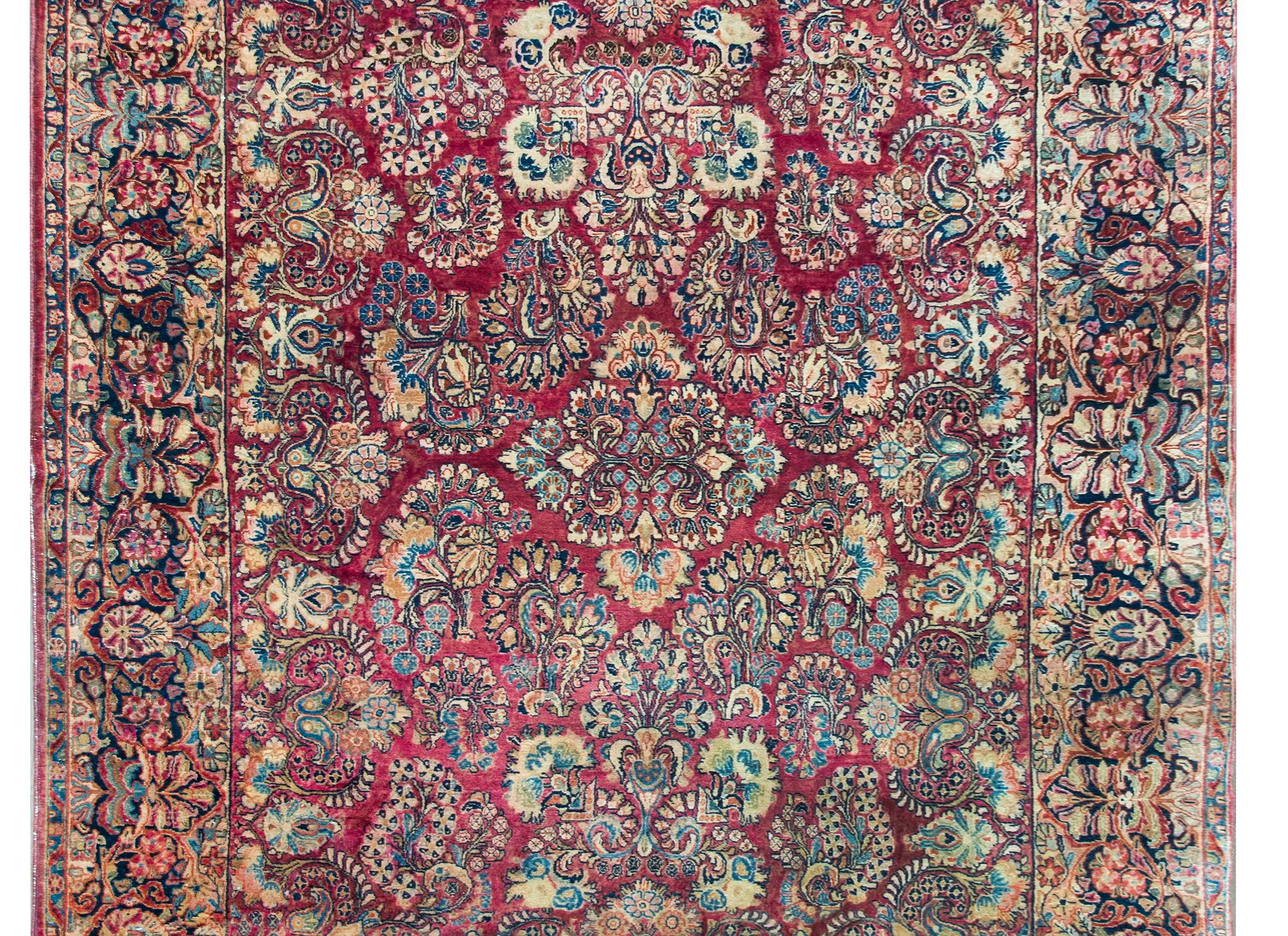 A beautiful early 20th century Persian Sarouk rug with an all-over large-scale mirrored floral cluster pattern with myriad flowers and leaves woven in tradition, Sarouk colors of light and dark indigo, cream, and pink set against a cranberry colored
