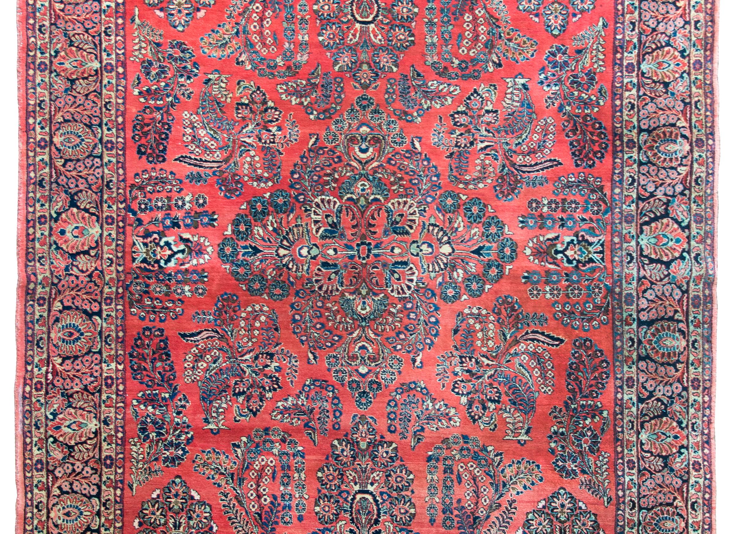 A beautiful early 20th century Persian Sarouk rug with an all-over mirrored floral cluster pattern with myriad flowers and woven in traditional Sarouk colors of light and dark indigo, cream, brown, pink, and all set against a crimson background. 