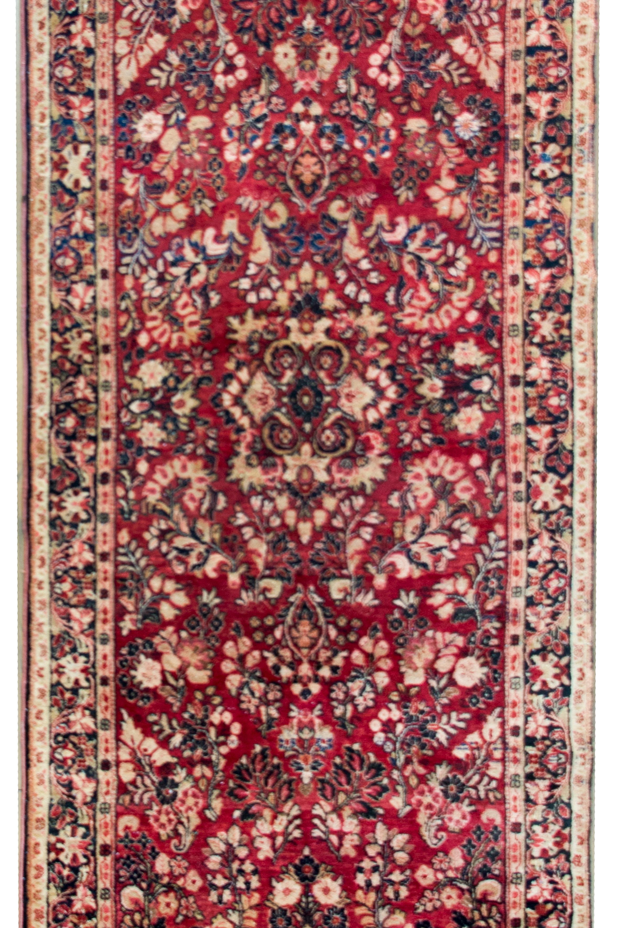 A classic early 20th century Persian Sarouk rug with an all-over mirrored pattern containing myriad floral clusters, surrounded by a complex border with a wide central floral patterned stripe flanked by a pair of petite floral patterned stripes, and