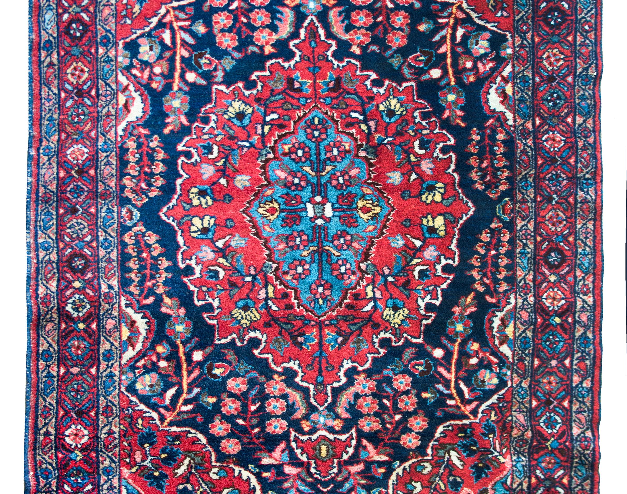 Un meraviglioso tappeto Sarouk persiano dell'inizio del XX secolo con un grande medaglione floreale centrale intrecciato con una miriade di fiori e viti a scorrimento, circondato da un bordo con un motivo floreale e di viti a scorrimento ripetuto,