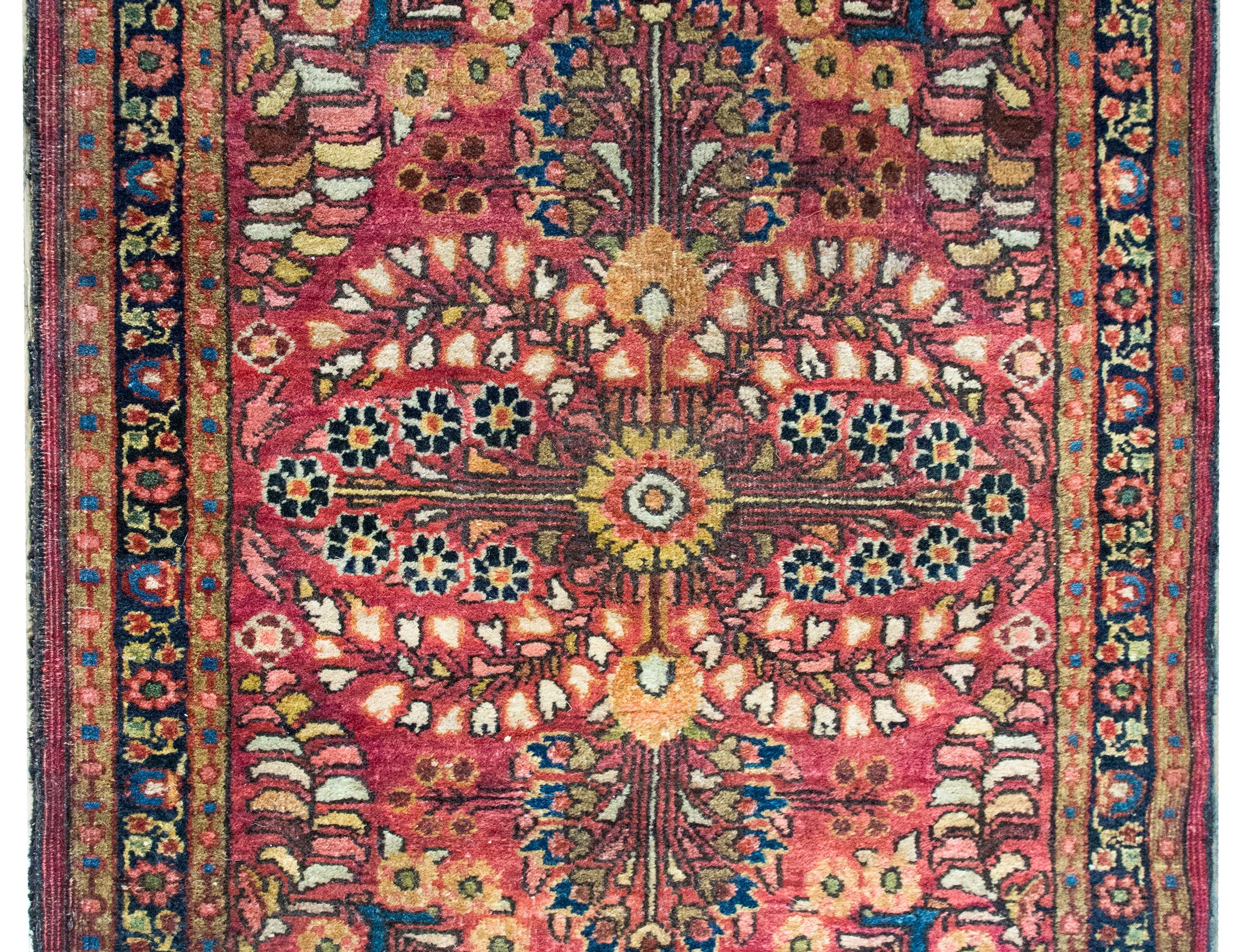 Un incantevole tappeto Sarouk persiano dei primi del Novecento con un motivo floreale a specchio, circondato da un semplice bordo con piccoli motivi floreali, il tutto tessuto nei toni del mirtillo rosso, dell'indaco, dell'oro e dell'arancione della