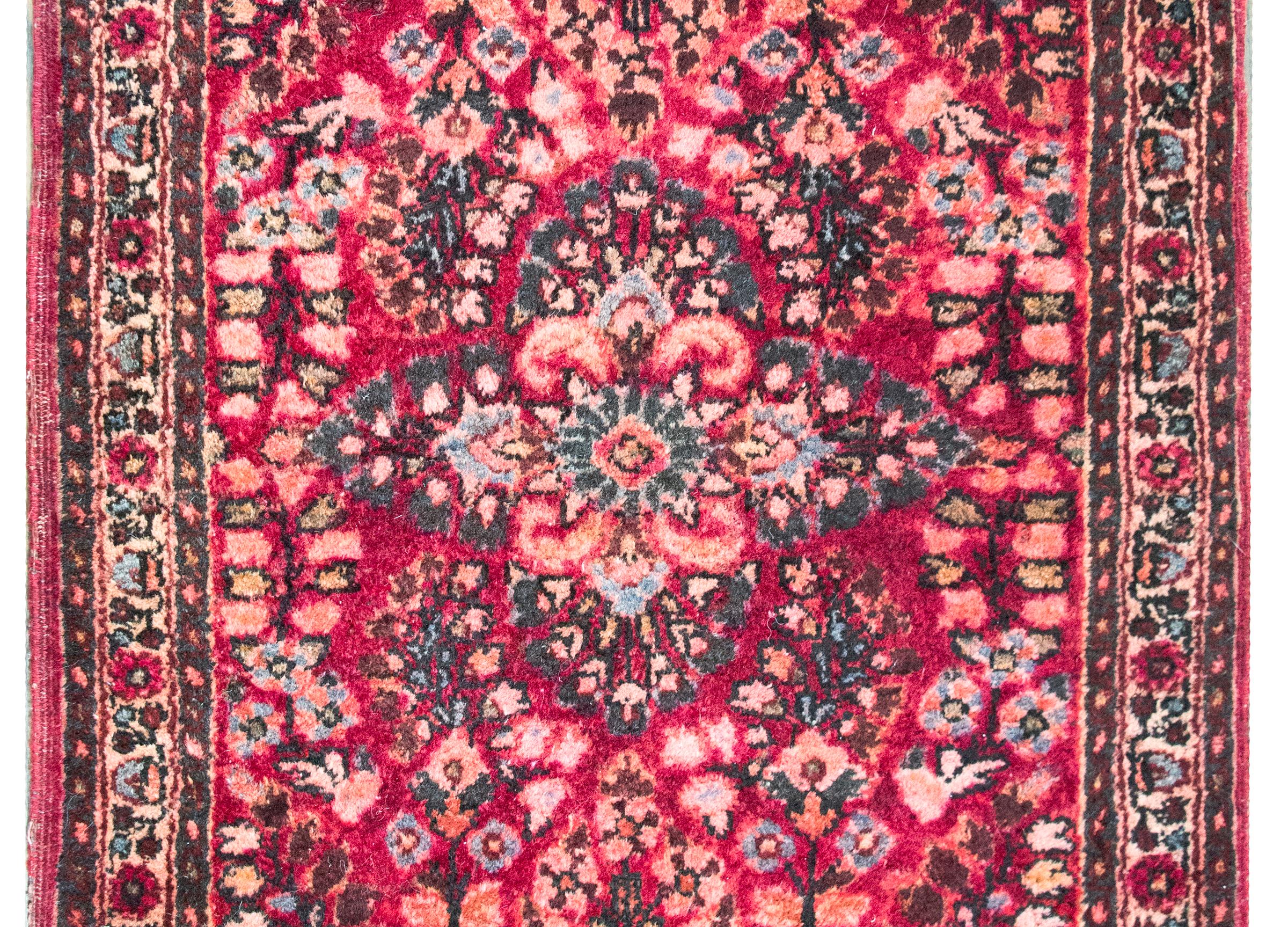 Encantadora alfombra persa Sarouk de principios del siglo XX con un medallón floral central que vive en un campo con un motivo floral reflejado, todo ello rodeado por un sencillo borde de motivos florales repetidos, y todo ello tejido en diversos