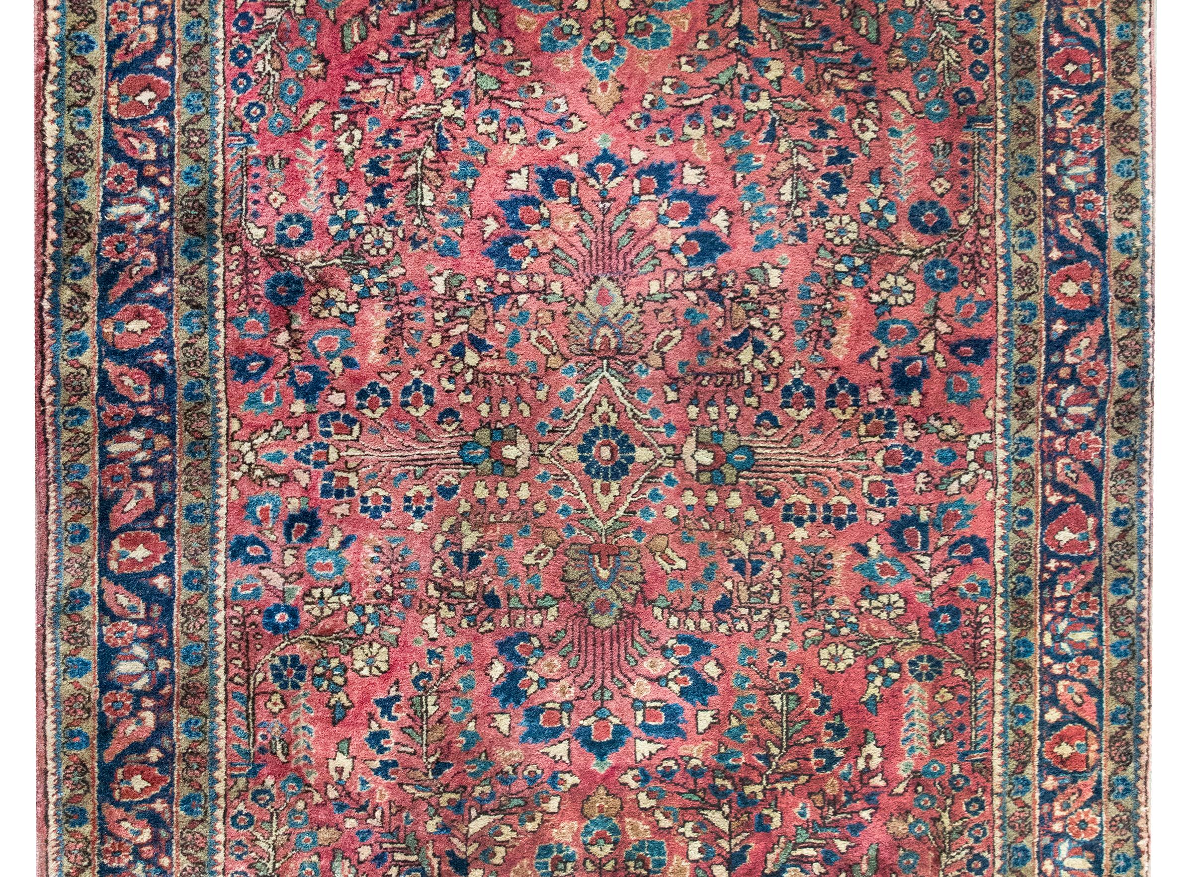 Un affascinante tappeto Sarouk persiano dei primi del Novecento con un tradizionale medaglione floreale centrale specchiato che vive in mezzo a un campo di altri grappoli di fiori, circondato da un ampio bordo con diverse piccole strisce a motivi