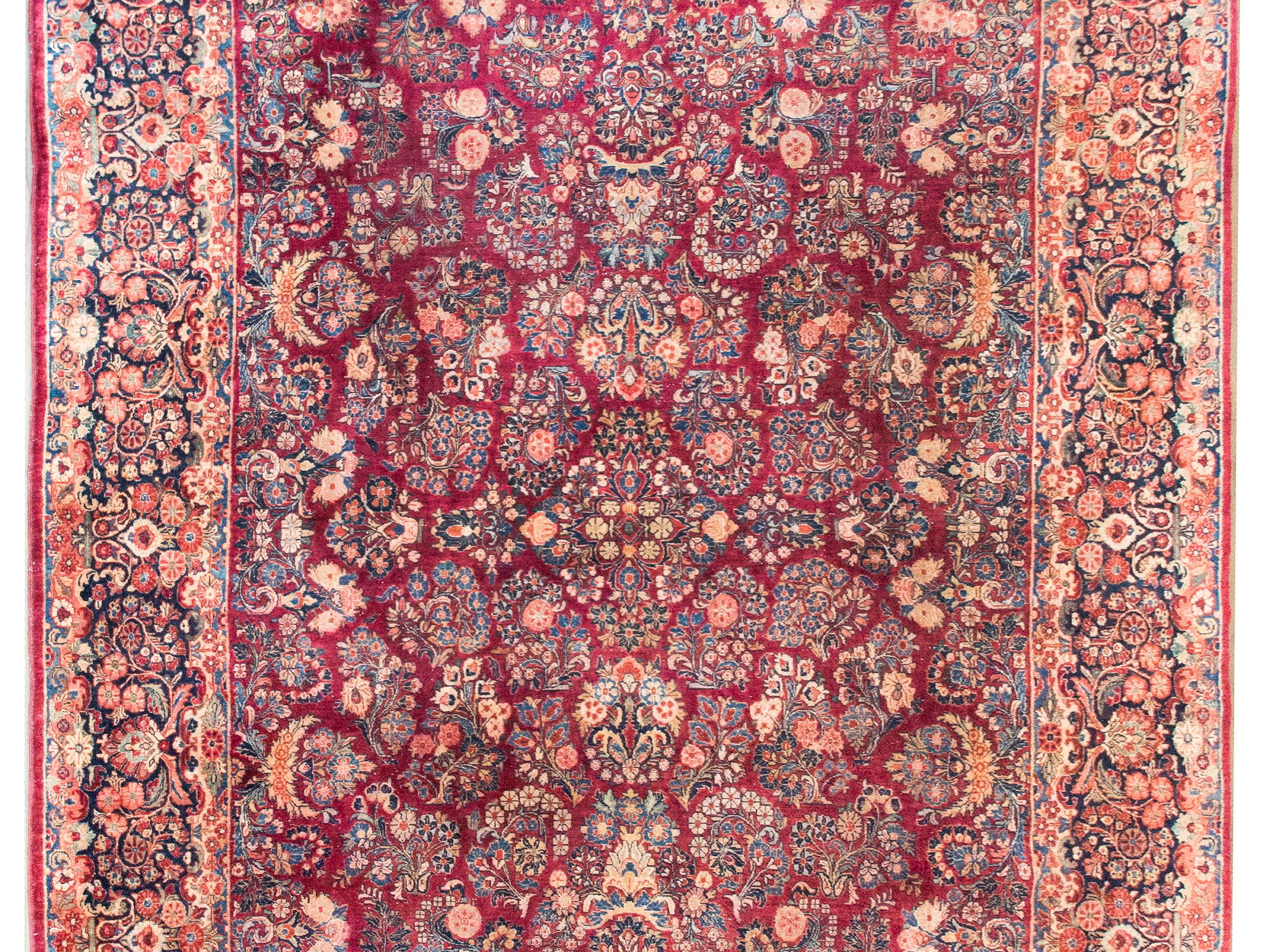 Questo splendido tappeto persiano Sarouk dei primi del Novecento è un'espressione senza tempo di eleganza classica e maestria artigianale. Il suo campo è ornato da un motivo all-over di grappoli floreali meticolosamente resi, specchiati