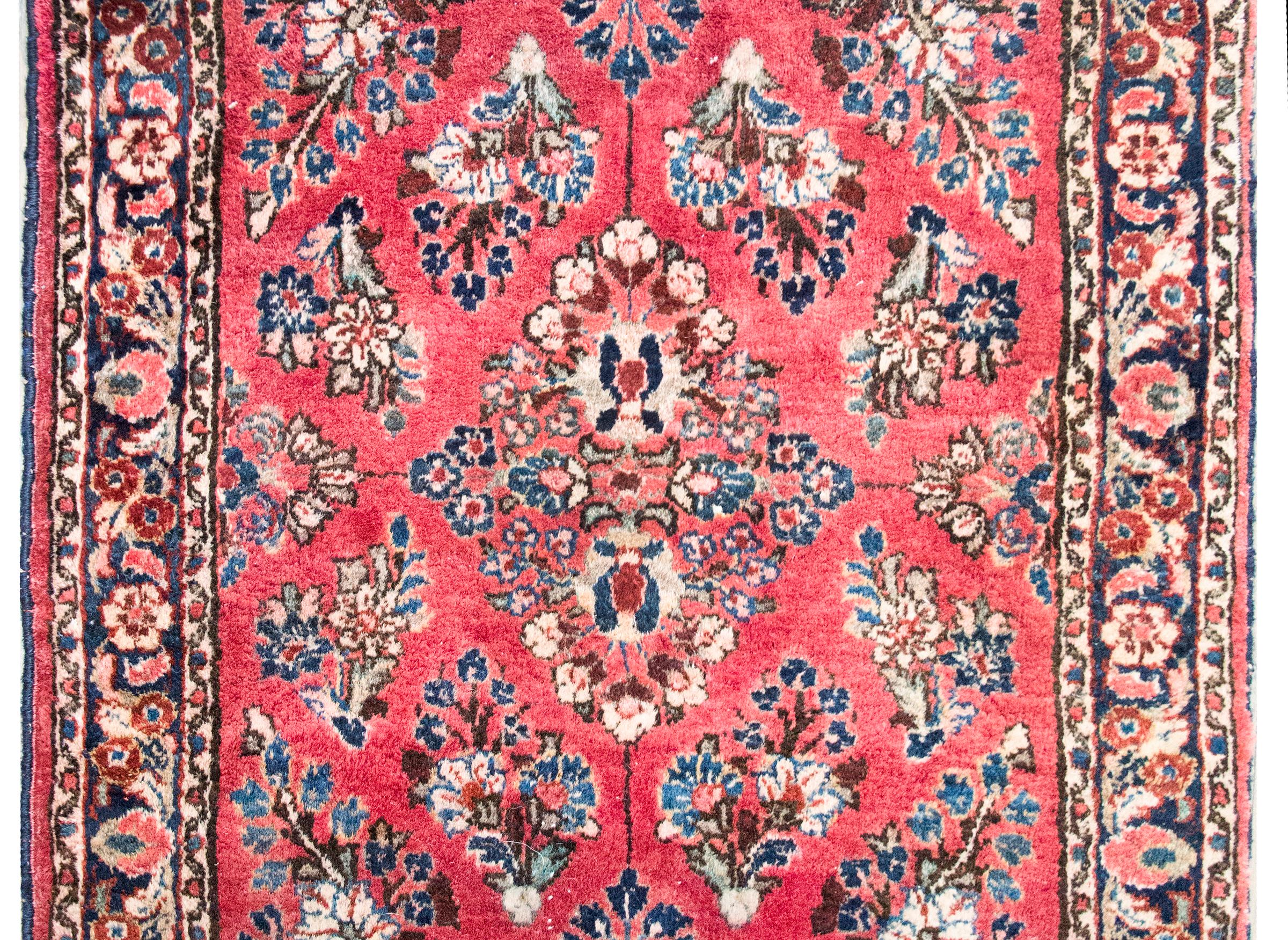 Un piccolo tappeto Sarouk persiano dell'inizio del XX secolo con un motivo floreale a specchio su tutto il campo, circondato da un semplice bordo con motivi floreali e viti a scorrimento, il tutto tessuto nei tradizionali colori Sarouk: mirtillo