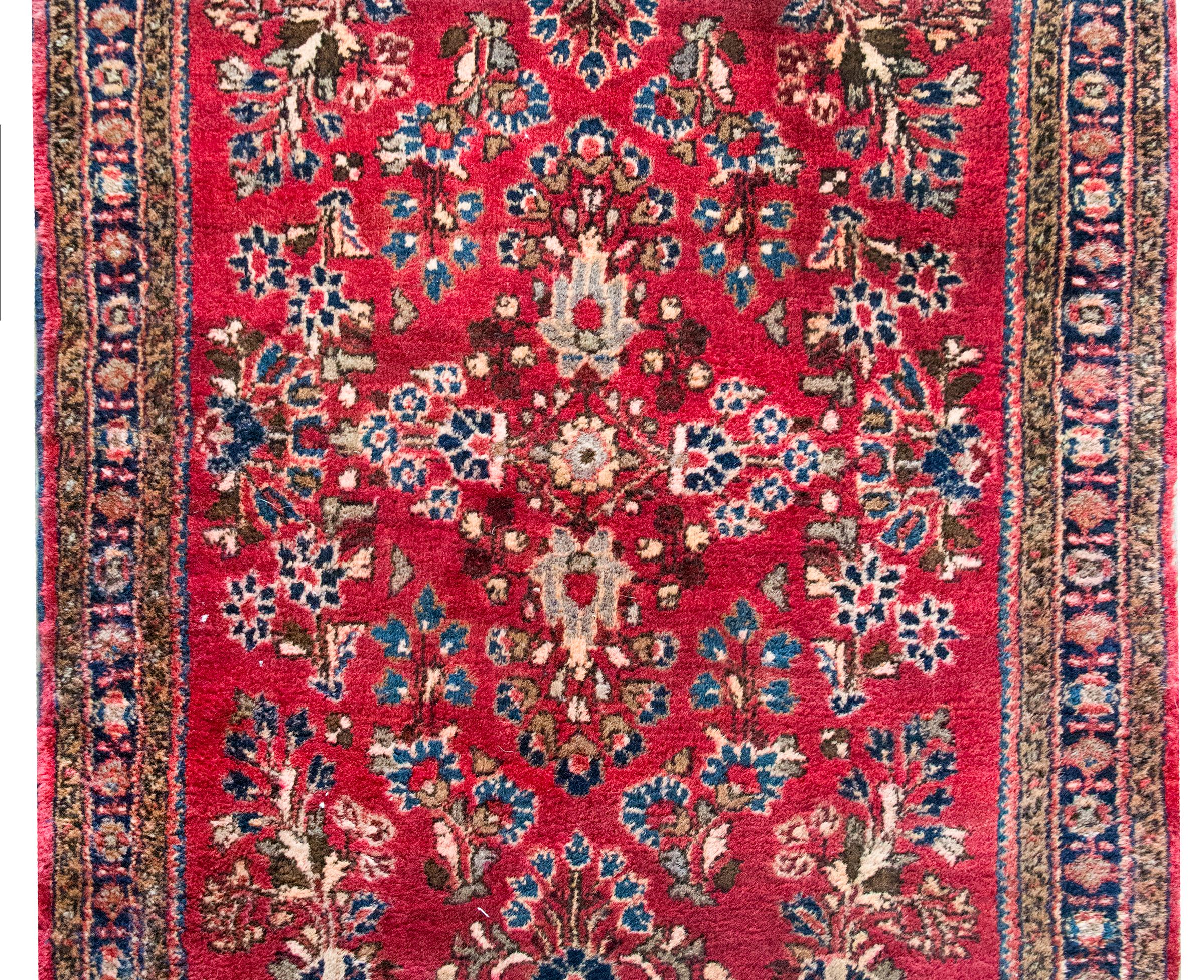 Un piccolo tappeto Sarouk persiano dell'inizio del XX secolo con un motivo floreale a specchio su tutto il campo, circondato da un semplice bordo con motivi floreali e viti a scorrimento, il tutto tessuto nei tradizionali colori Sarouk: mirtillo