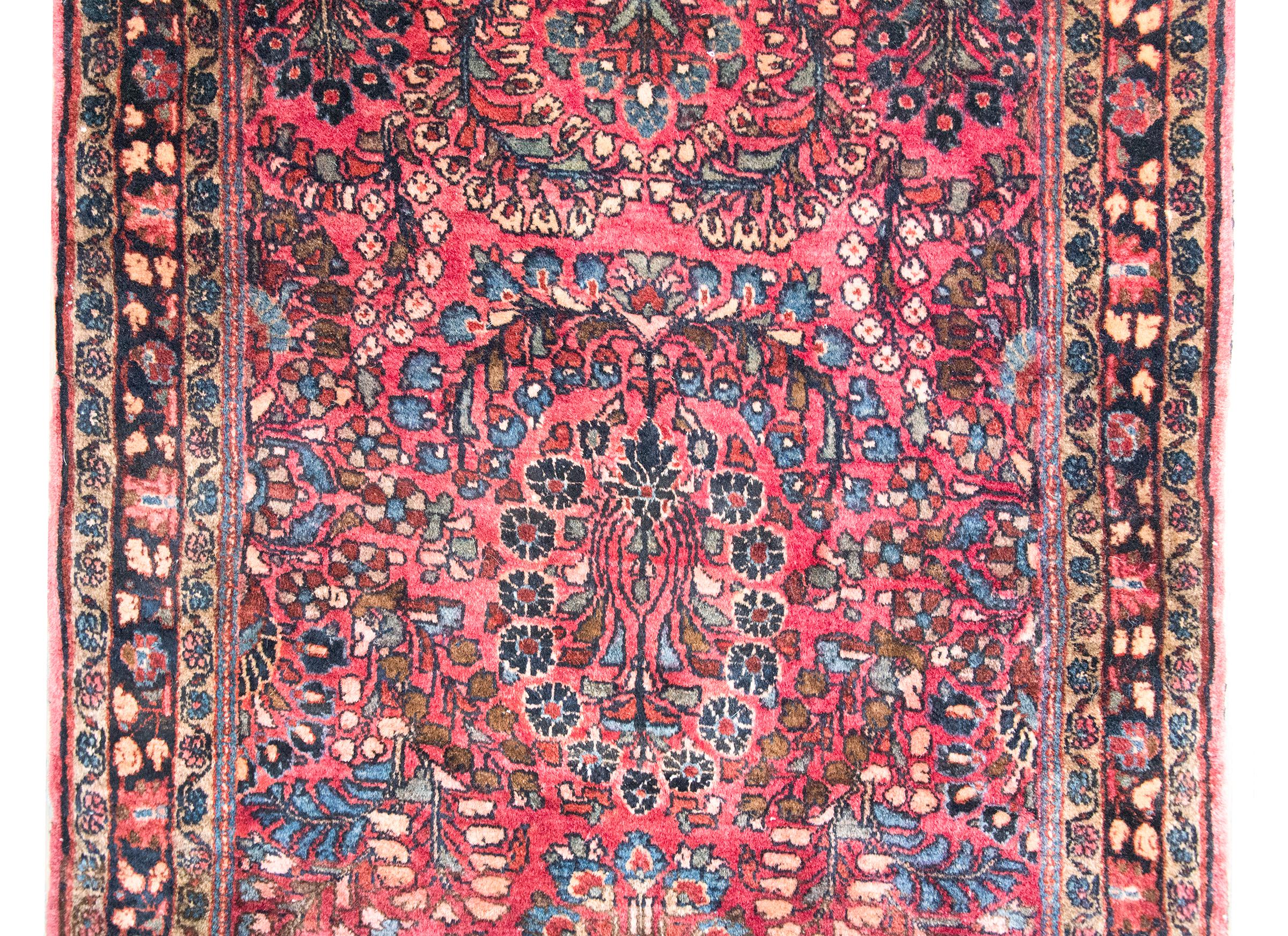 Un bellissimo tappeto Sarouk persiano dell'inizio del XX secolo con un motivo floreale a specchio circondato da un bordo complesso con diverse strisce a motivo floreale e a vite che scorrono, il tutto tessuto nei tradizionali colori Sarouk: mirtillo