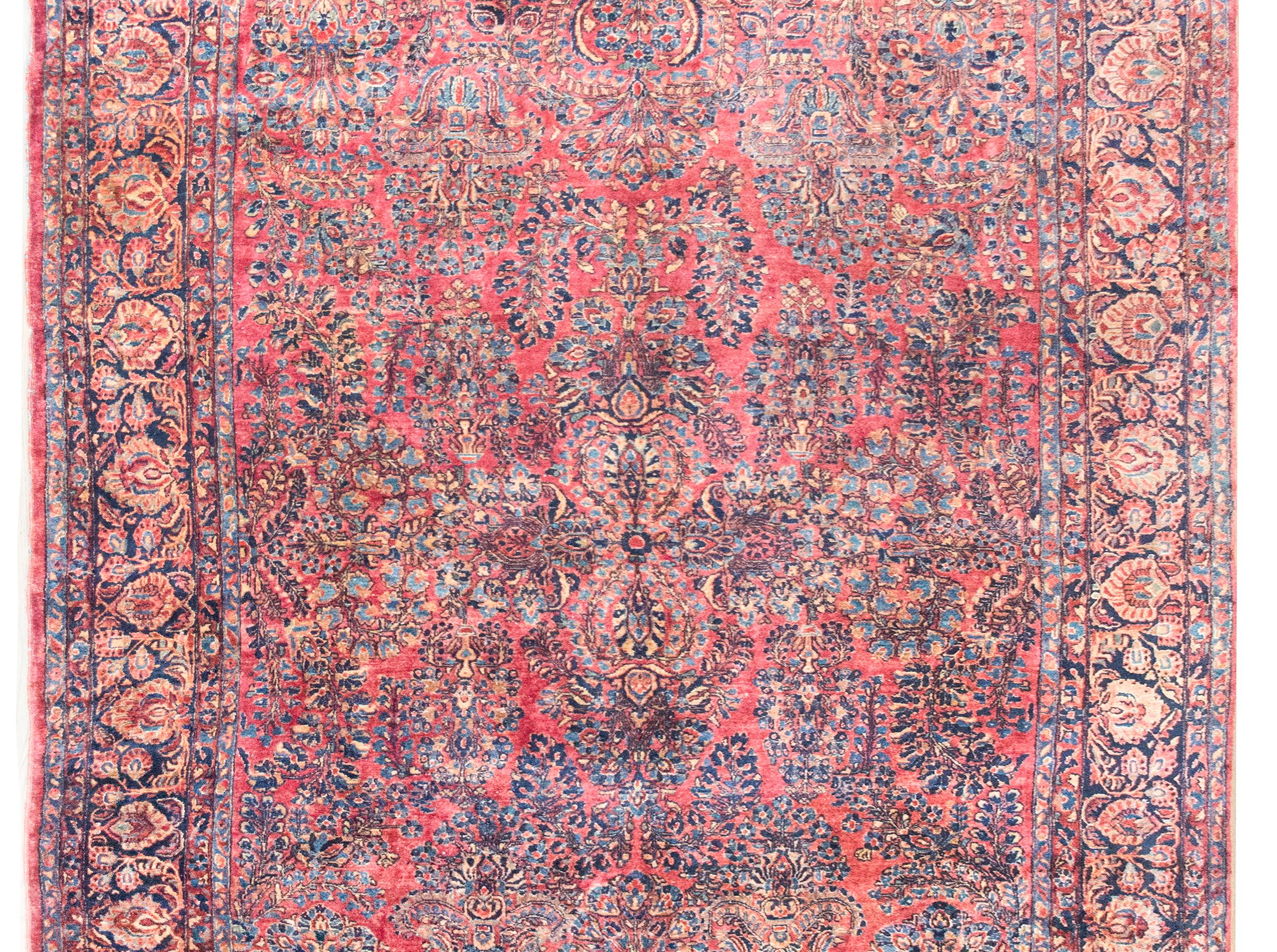 Uno splendido tappeto Sarouk persiano di grandi dimensioni dell'inizio del XX secolo con un motivo a specchio all-over con una miriade di grappoli floreali e tralci che scorrono, circondato da un ampio bordo complesso con un'ampia striscia centrale