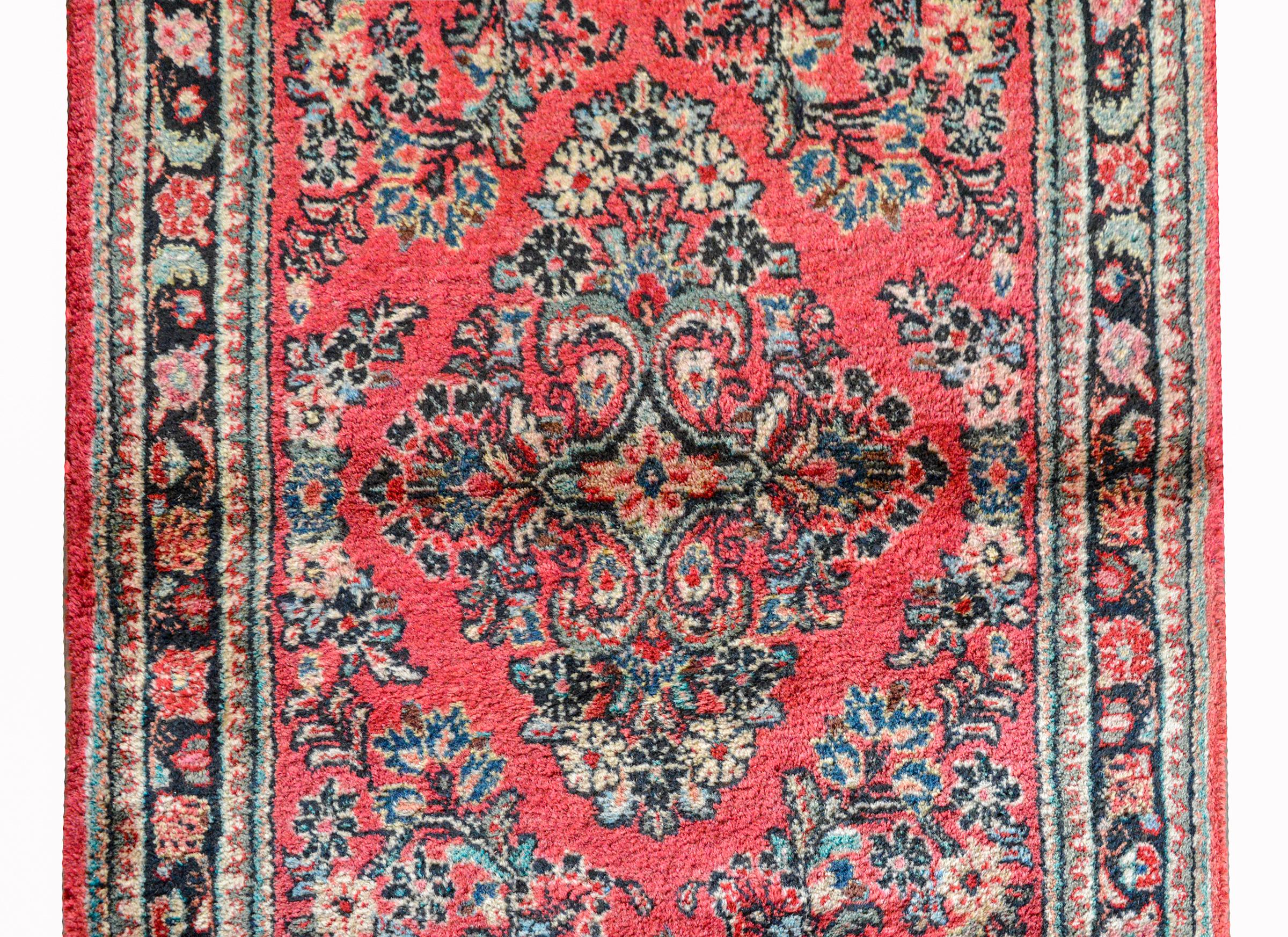 A wonderful early 20th century Persian Sarouk runner with a traditional all-over mirrored floral pattern woven in pink, indigo, and cream, set against a dark cranberry background and surrounded by multiple petite floral patterned stripes.