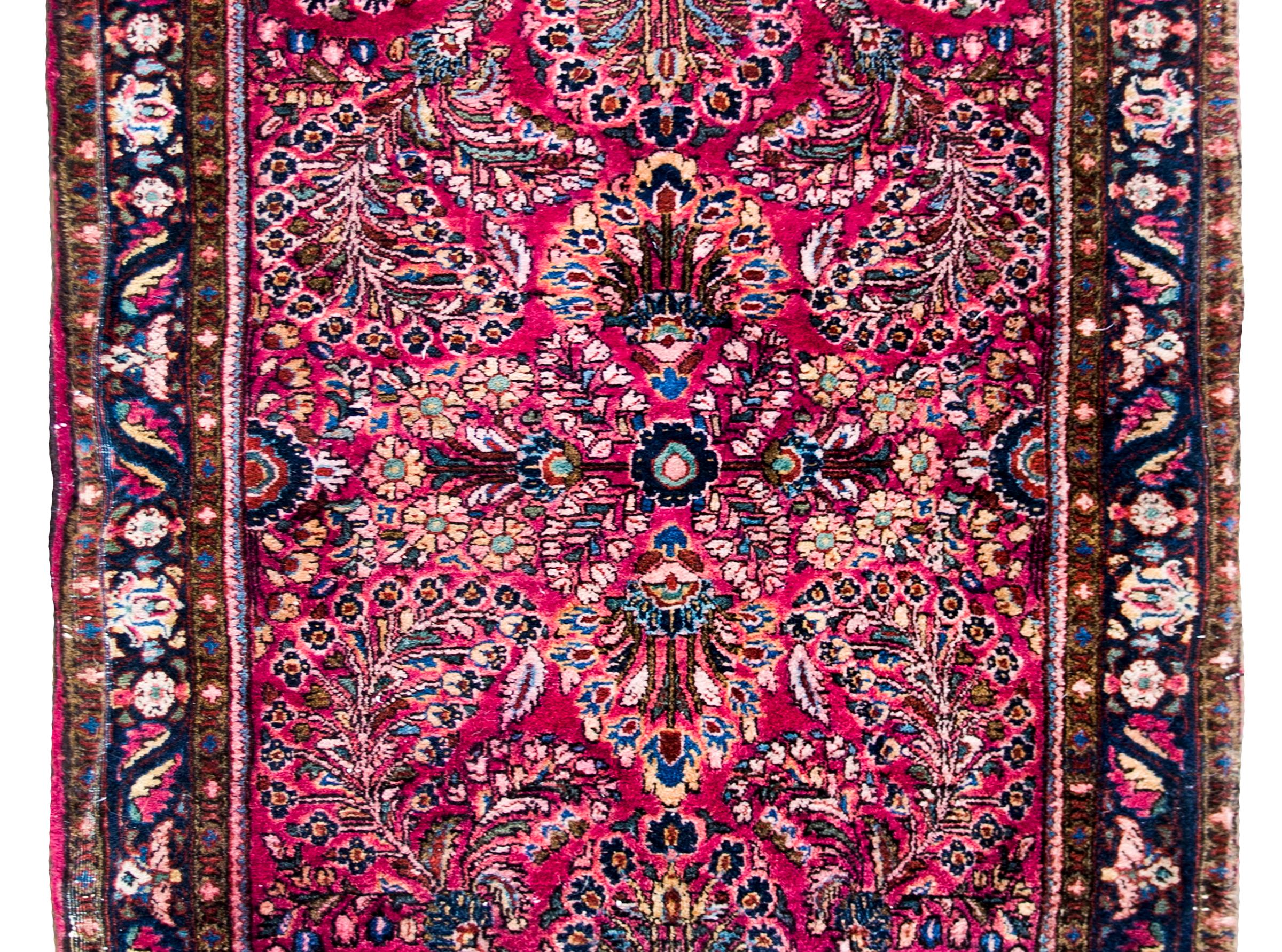 A beautiful early 20th century Persian Sarouk runner with a large-scale mirrored floral pattern containing myriad floral clusters all woven in light and dark indigo, pink, white, and olive green set against a brilliant cranberry background, and