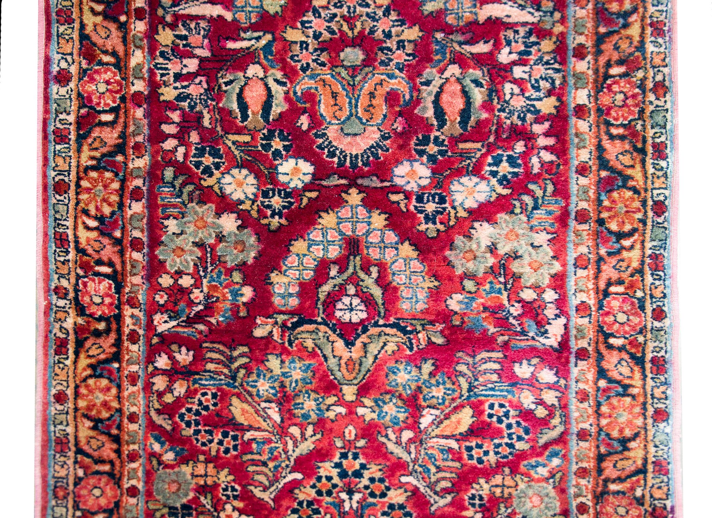 A wonderful early 20th century Persian Sarouk runner with an all-over mirrored floral pattern woven in traditional Sarouk colors of cranberry, pink, light and dark indigo, and cream, and all surrounded by a border with multiple large and small scale