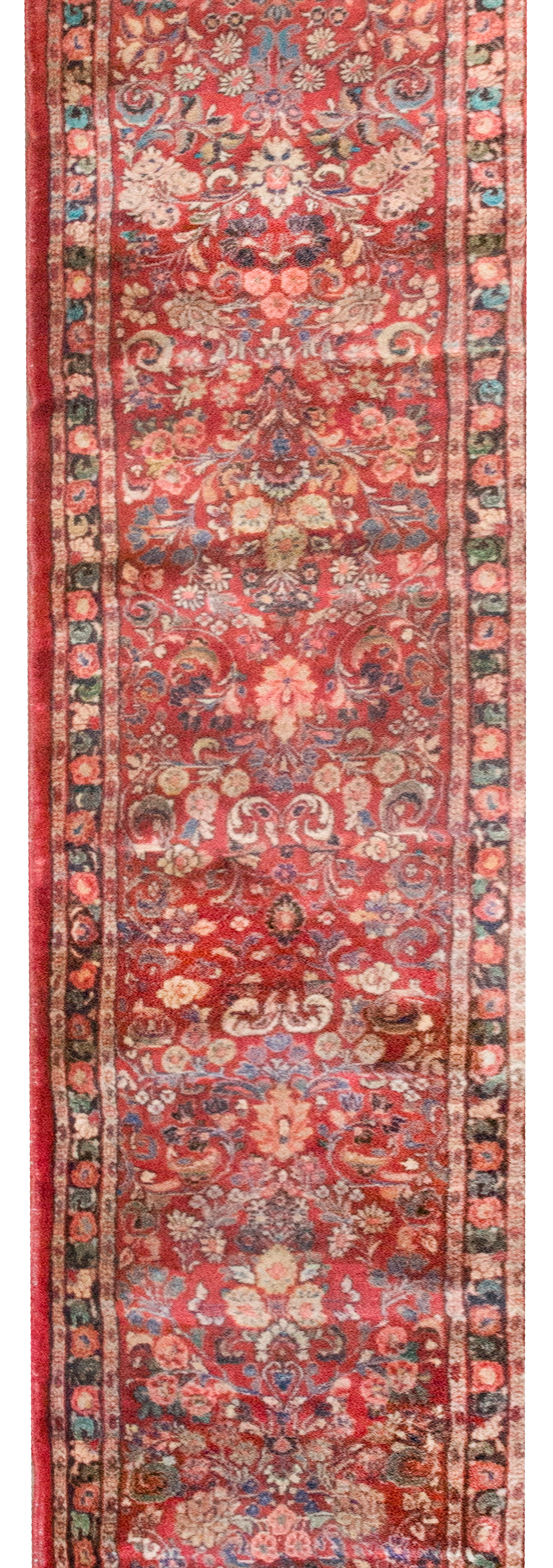 This early 20th-century Persian Sarouk runner features a classic mirrored floral pattern, richly woven in shades of cranberry, cream, pink, and light and dark indigo. The central field blooms with stylized sprays and palmettes arranged in