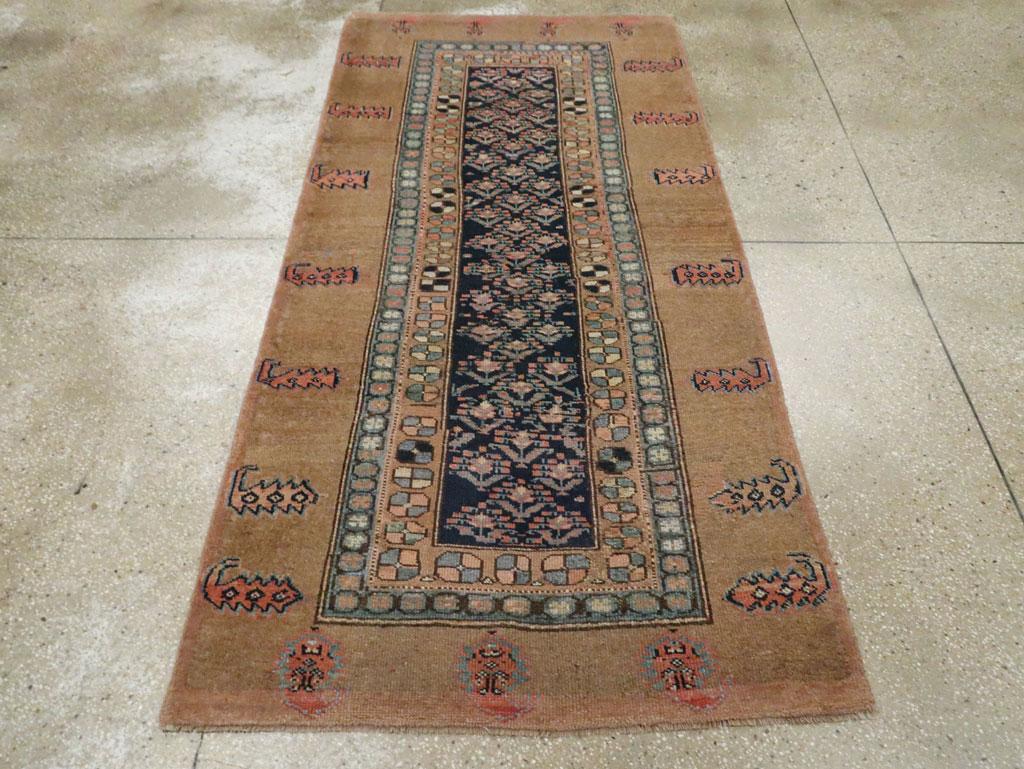 Una alfombra de acento persa Serab vintage. Un ancho borde de tono camel cálido tiene botes dentados muy espaciados y encierra un estrecho campo azul oscuro con un 2-1-2. Patrón floral de media gota. Un colorido borde interior de octógonos