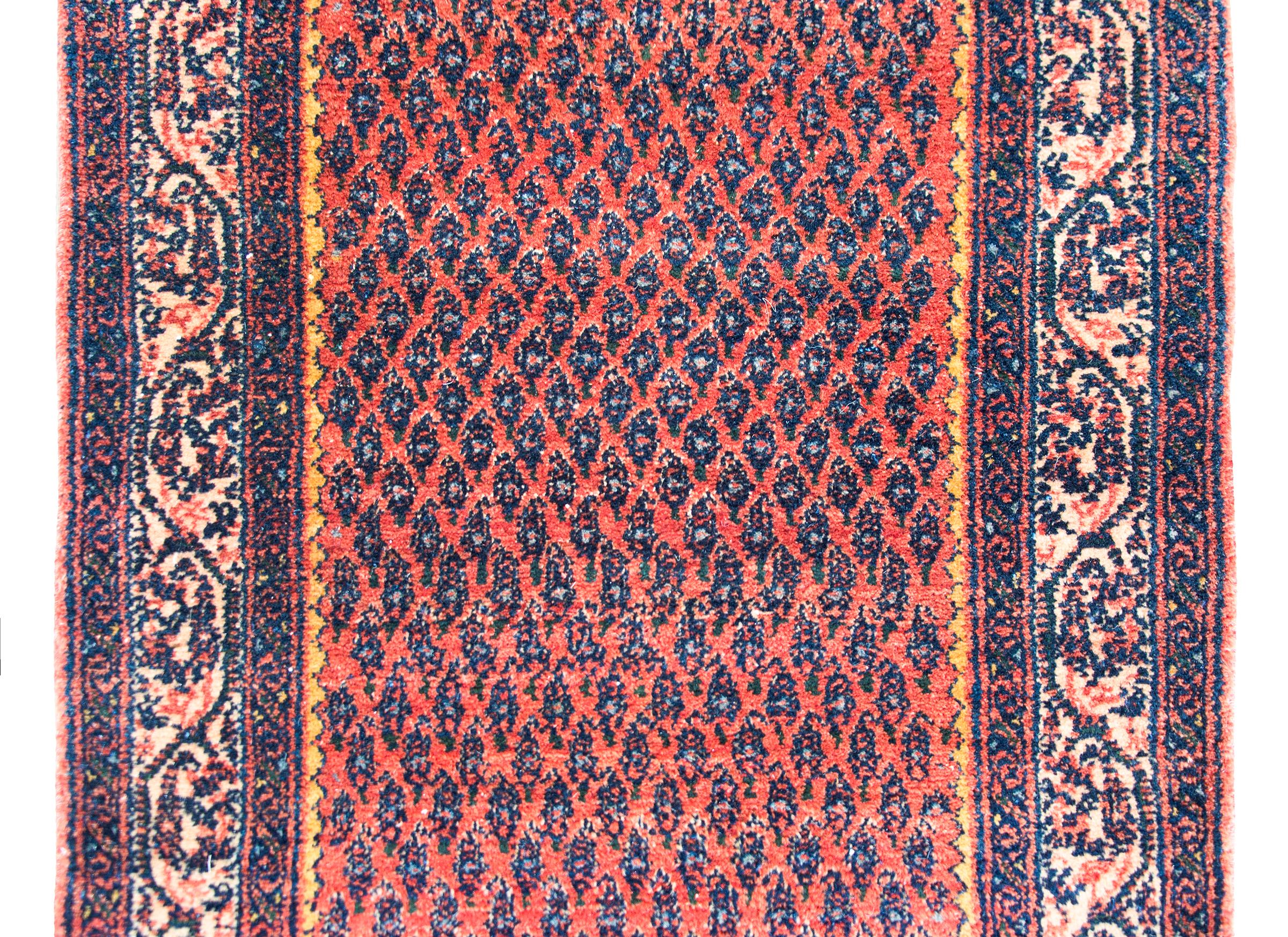 An early 20th century Persian Seraband runner with an all-over paisley pattern surrounded by a wide paisley patterned border and all woven light and dark indigo gold and pink, set against an abrash crimson background.