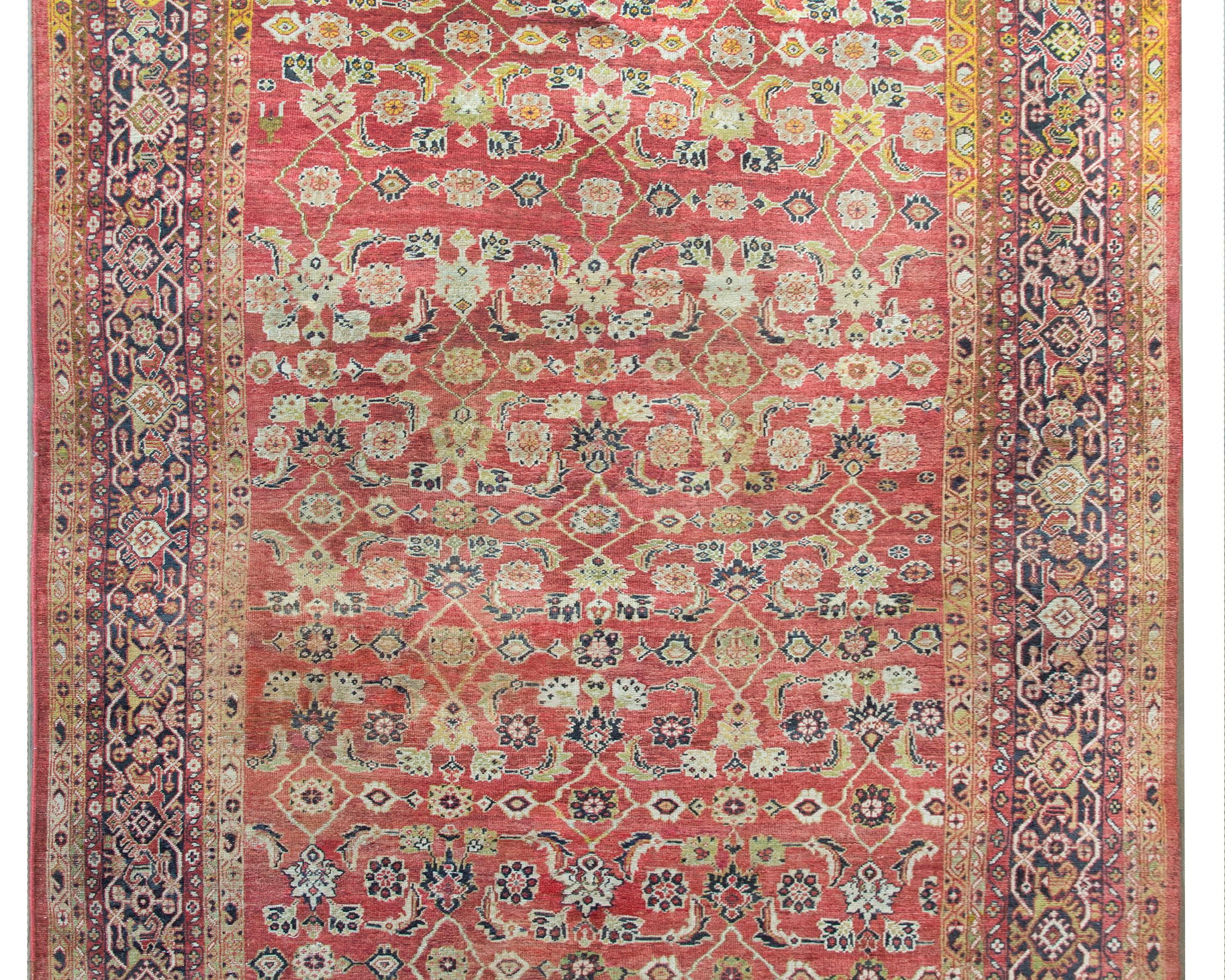 A stunning early 20th century Persian Sultanabad rug with a fantastic all-over pattern with myriad stylized flowers and leaves woven in gold, cream, pink, and brown set against a coral background.  The border is exceptional with seven distinct