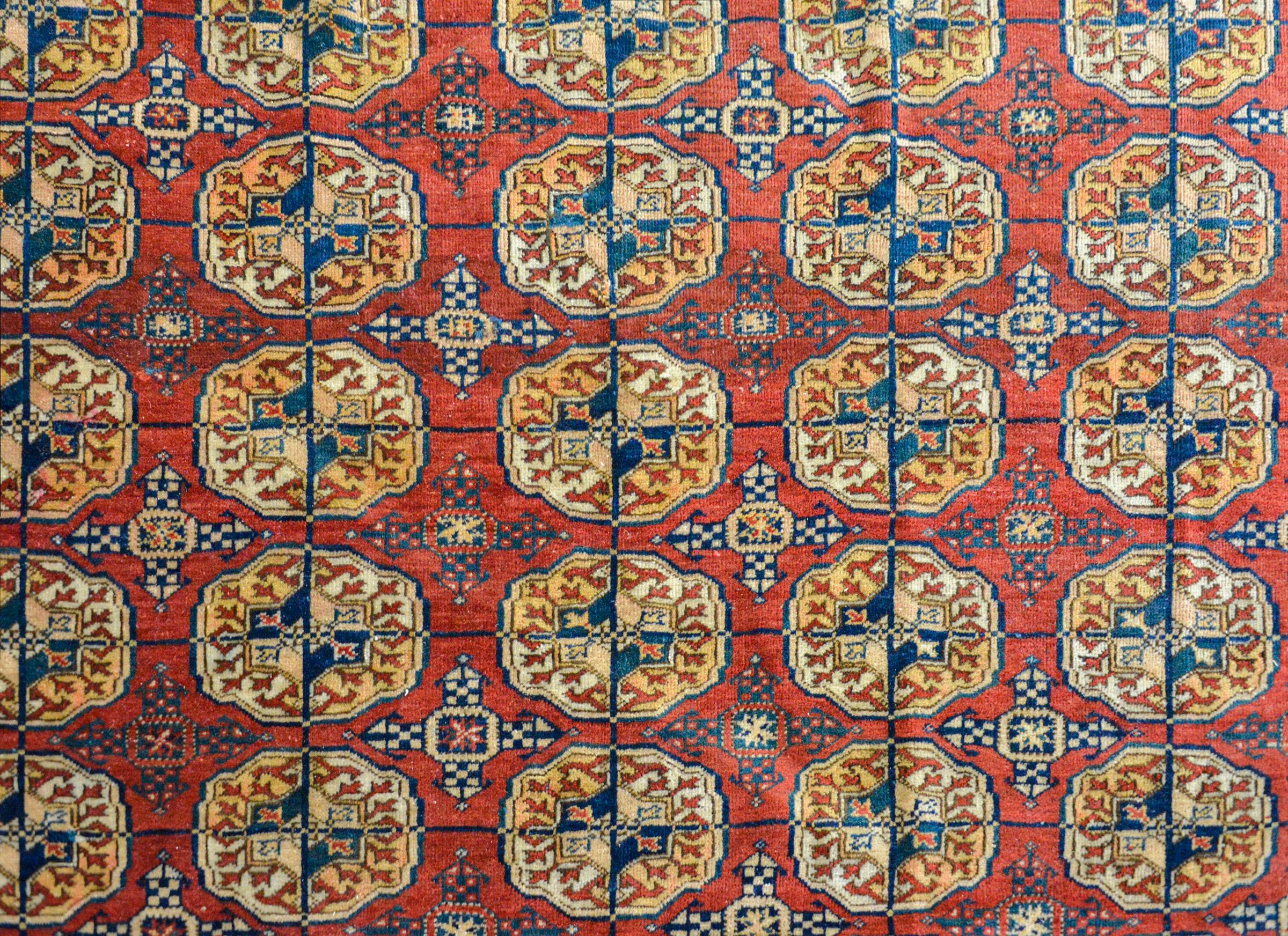 Ein wunderbarer persischer Tekeh-Teppich aus dem frühen 20. Jahrhundert mit einem Allover-Muster aus stilisierten Blumenmedaillons in Gold, Creme, Indigo und Karminrot auf einem karminroten Feld mit weiteren stilisierten Blumen. Die Bordüre ist
