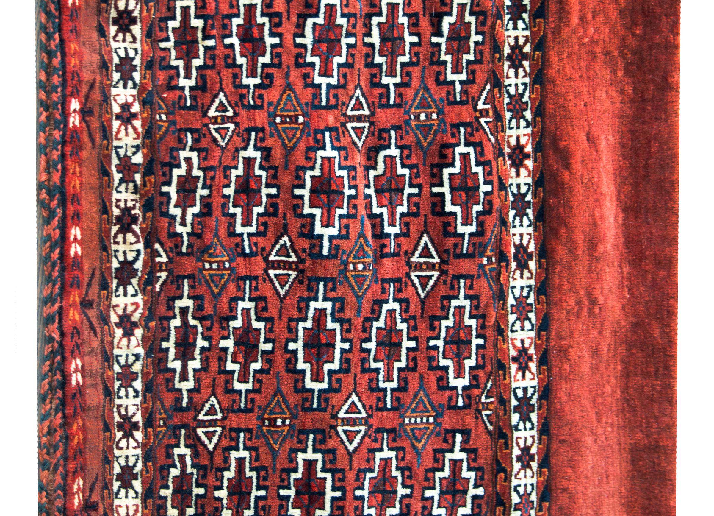 A charming early 20th century Persian Yamut bag face rug with an all-over pattern with diamonds and stylized flowers woven in light and dark indigo, orange, and crimson, and surrounded by a border of multiple thin stylized geometric patterned