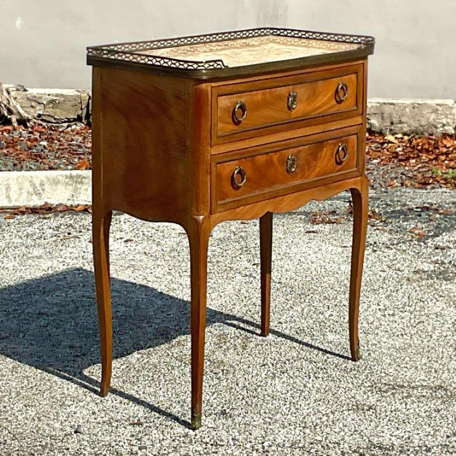 Vintage petite marble top commode with brass rail trim around the top of commode with two drawers featuring brass trim around the inlay and round drop handles. Acquired from a Palm Beach estate.