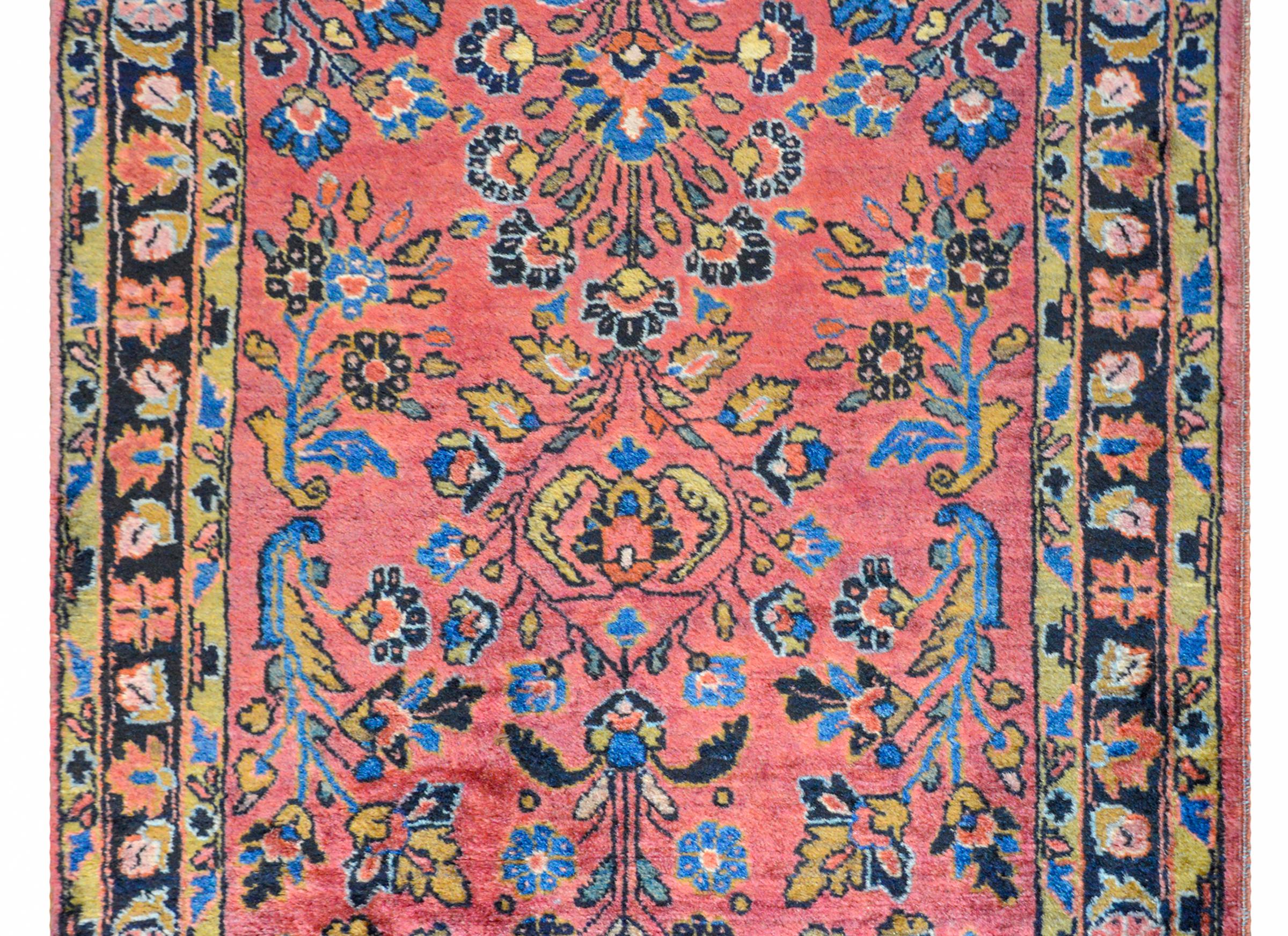 A wonderful early 20th century Persian petite Sarouk rug with a beautiful floral and scrolling vine pattern woven in light and dark indigo, gold, and coral on a pale cranberry background. The border is composed of a central floral patterned stripe