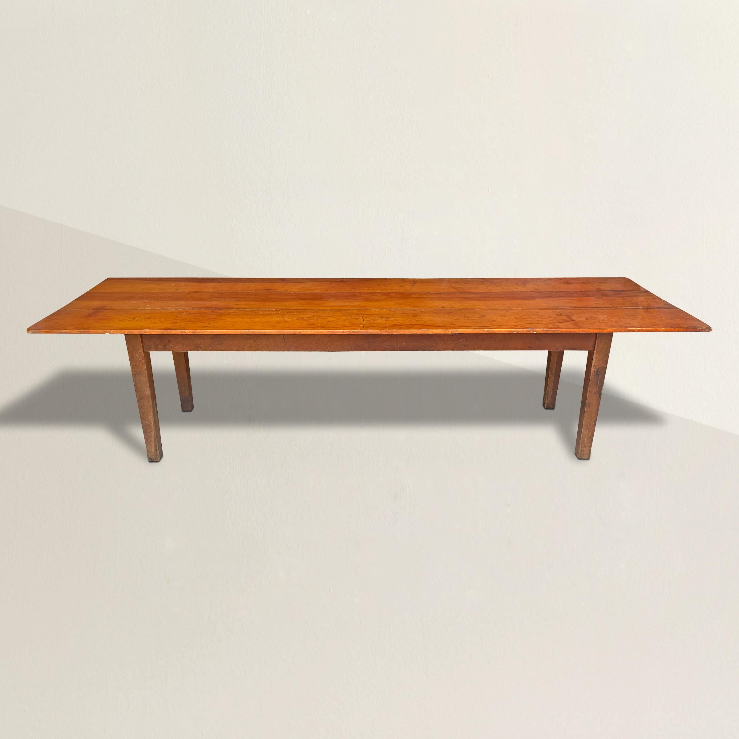 A simple early 20th century American Shaker-inspired ten-foot long pine harvest table with three wide boards on top, and simple tapered square legs.