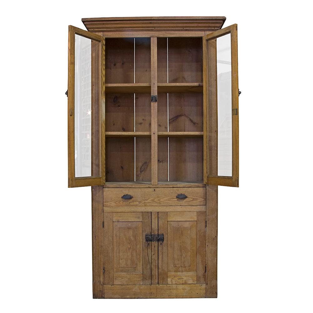 This early 20th century cabinet is solid pine and retains its original hardware and glass. The piece is beautifully made and has an earthy patina that pairs well with any decor. The cabinet has three shelves in its upper, a single central drawer,