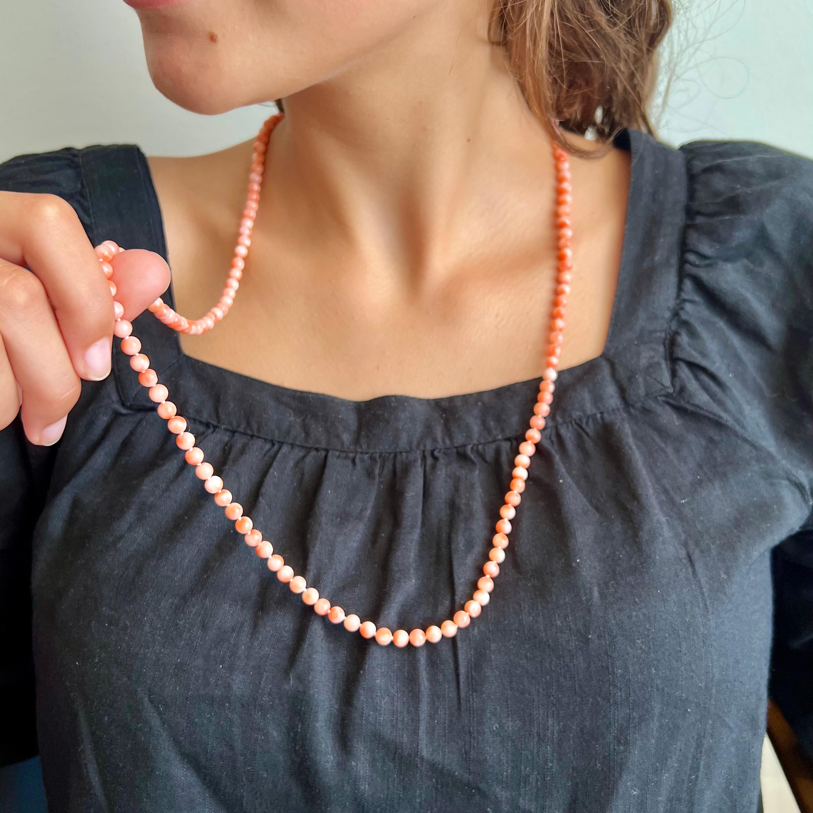 An Art Deco natural pink coral 14 karat gold single-strand beaded necklace. The coral beads of this necklace are round-shaped and are beautifully mottled with different hues of red and pink. The round openwork and scalloped gold clasp is set with a