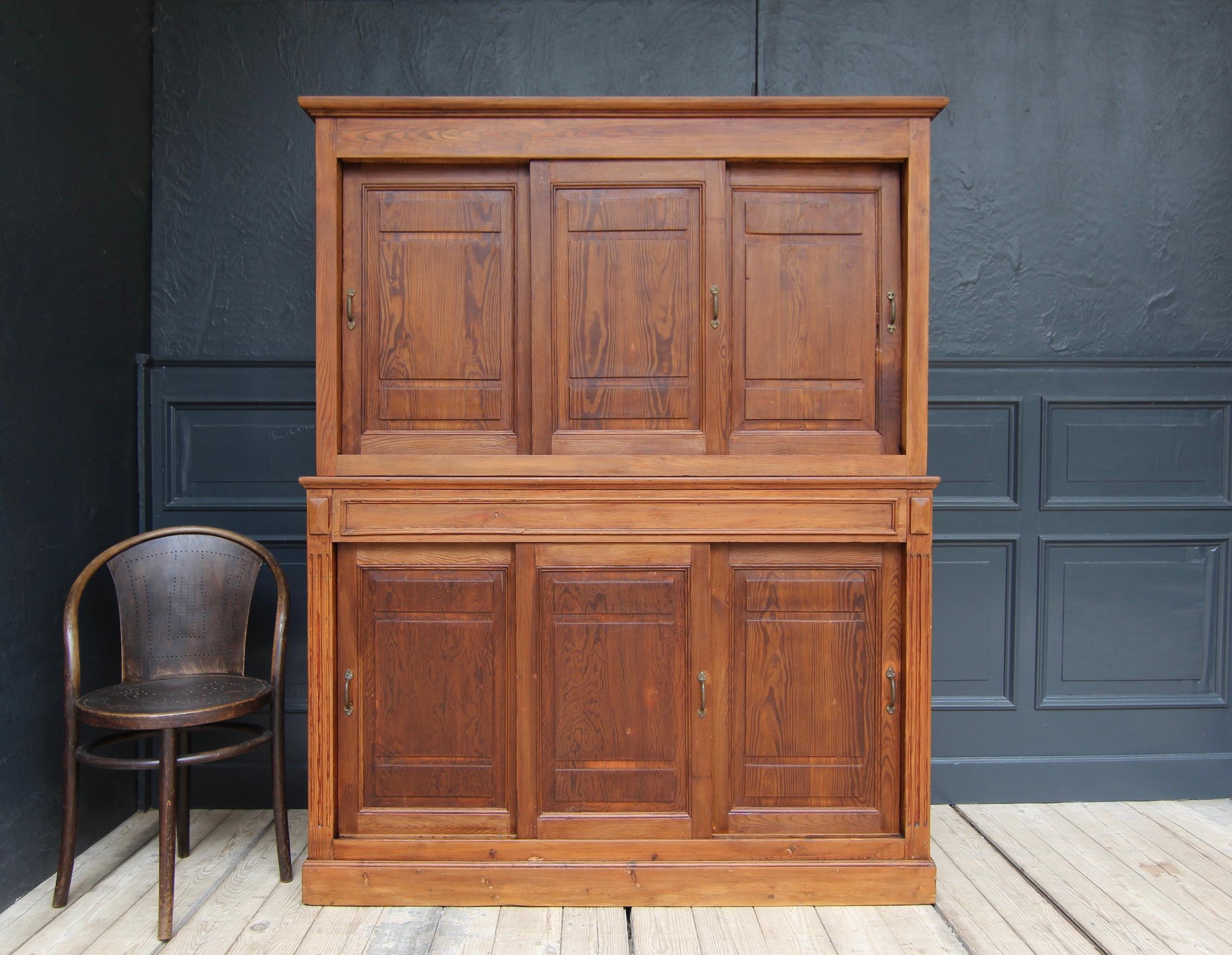 Vintage sliding door cabinet from the early 20th century. Made in Pitch Pine wood. 

Consisting of a lower and an upper cabinet, each with 3 sliding doors made in frame construction.

Original brass handles mounted.

Fitted with 3 shelves inside (1
