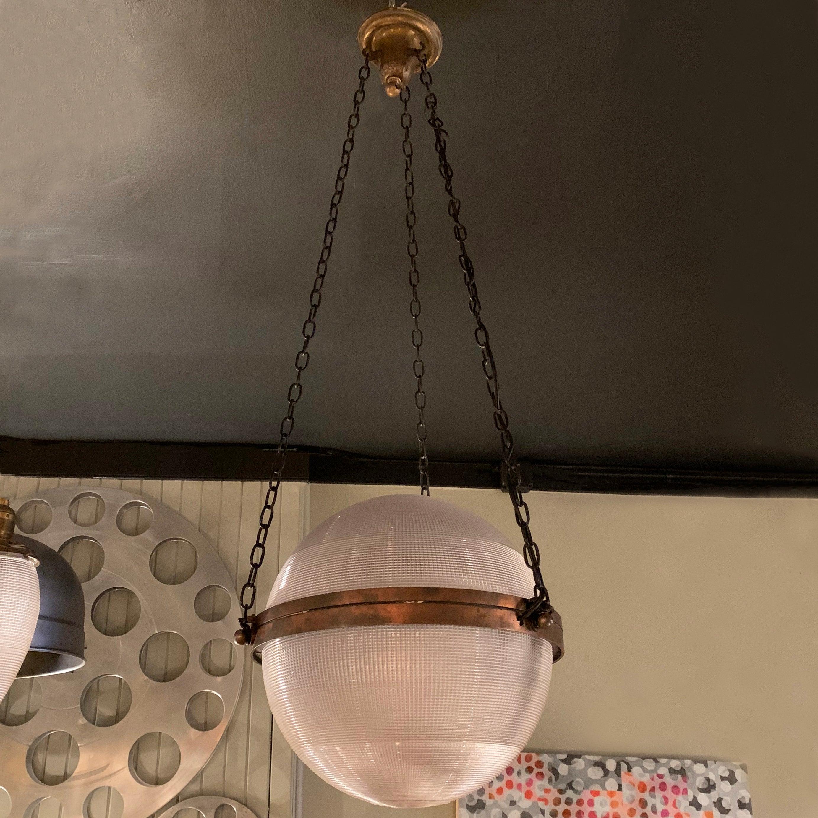 Outstanding, large, early 20th century, pharmacy pendant light features a 12 inch diameter, prismatic, Holophane glass globe shade with brass band suspended with 3 chains from a matching brass canopy. The pendant is newly wired to accept up to a 200