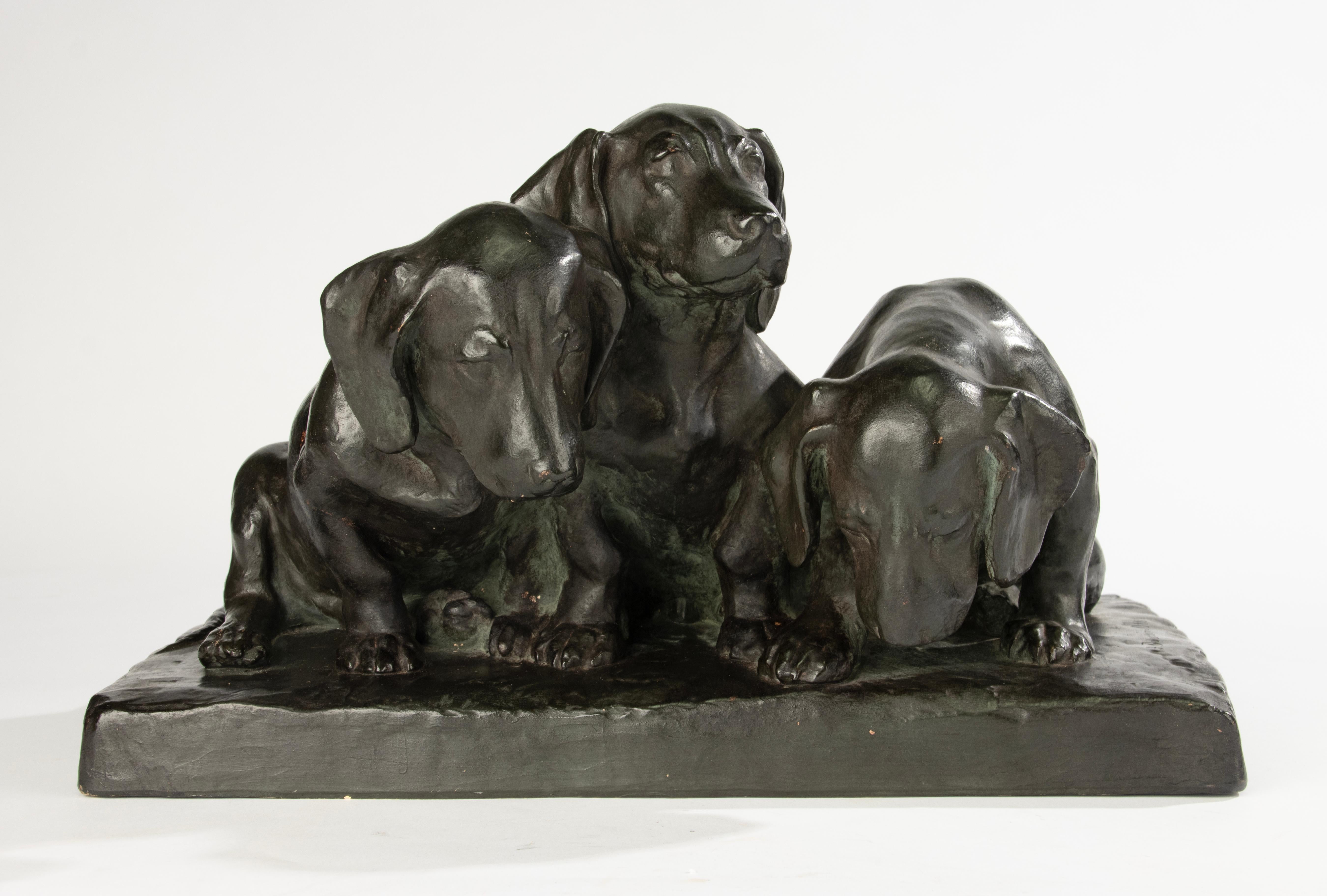 Charmante patinierte Terrakotta-Skulptur, die drei eng beieinander sitzende Dackelwelpen darstellt, die Wärme und Unschuld ausstrahlen. Entworfen von Jenny von Barry Poussin Ott und mit der Herstellermarke von Keram versehen. Kunstwerkstätte Schön &