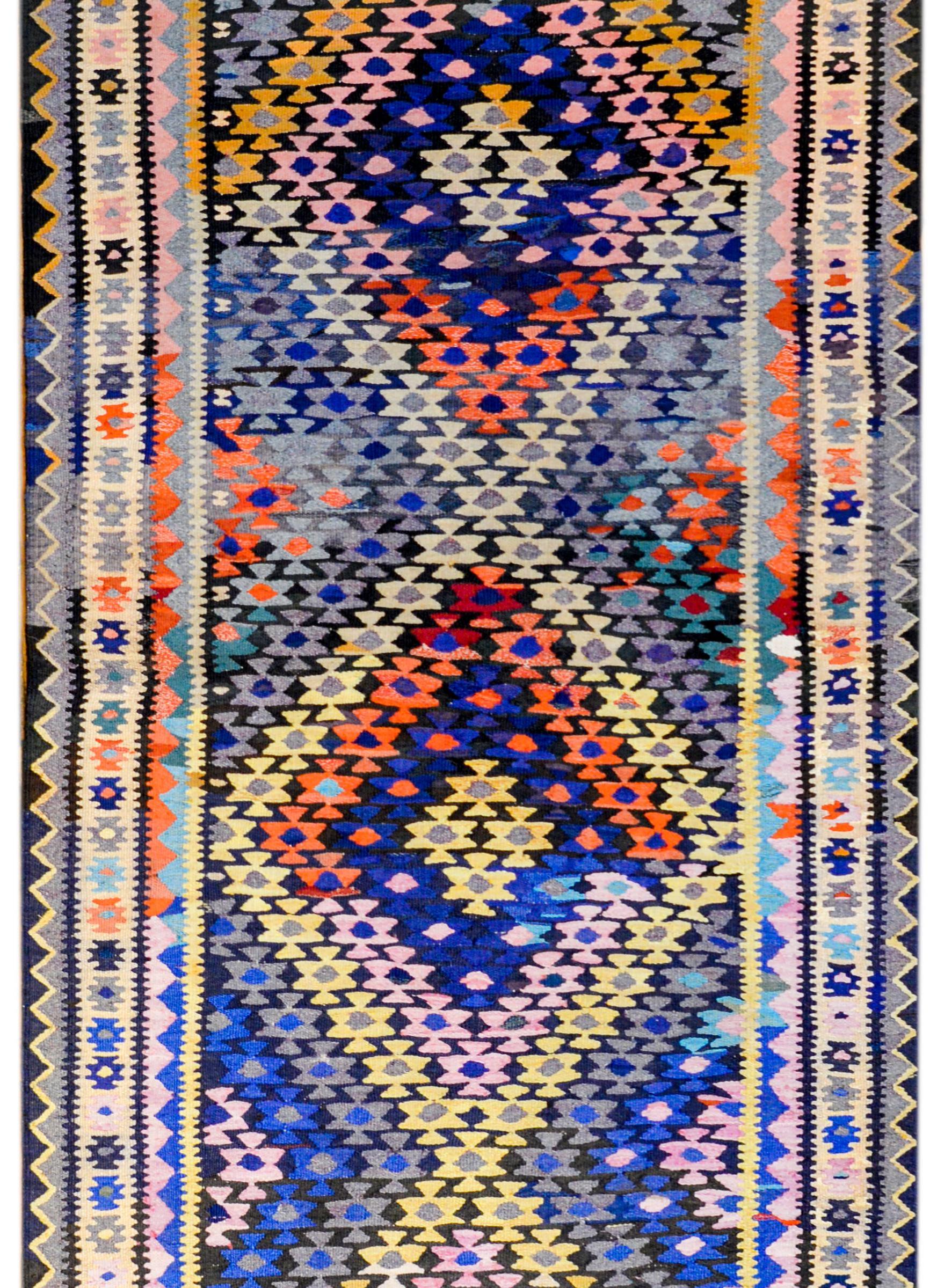 An early 20th century Persian Qazvin Kilim rug with an all-over stylized floral pattern woven in myriad colors in a way that a large-scale zigzag pattern is created across the field. The border is complementary with a central stylized floral pattern