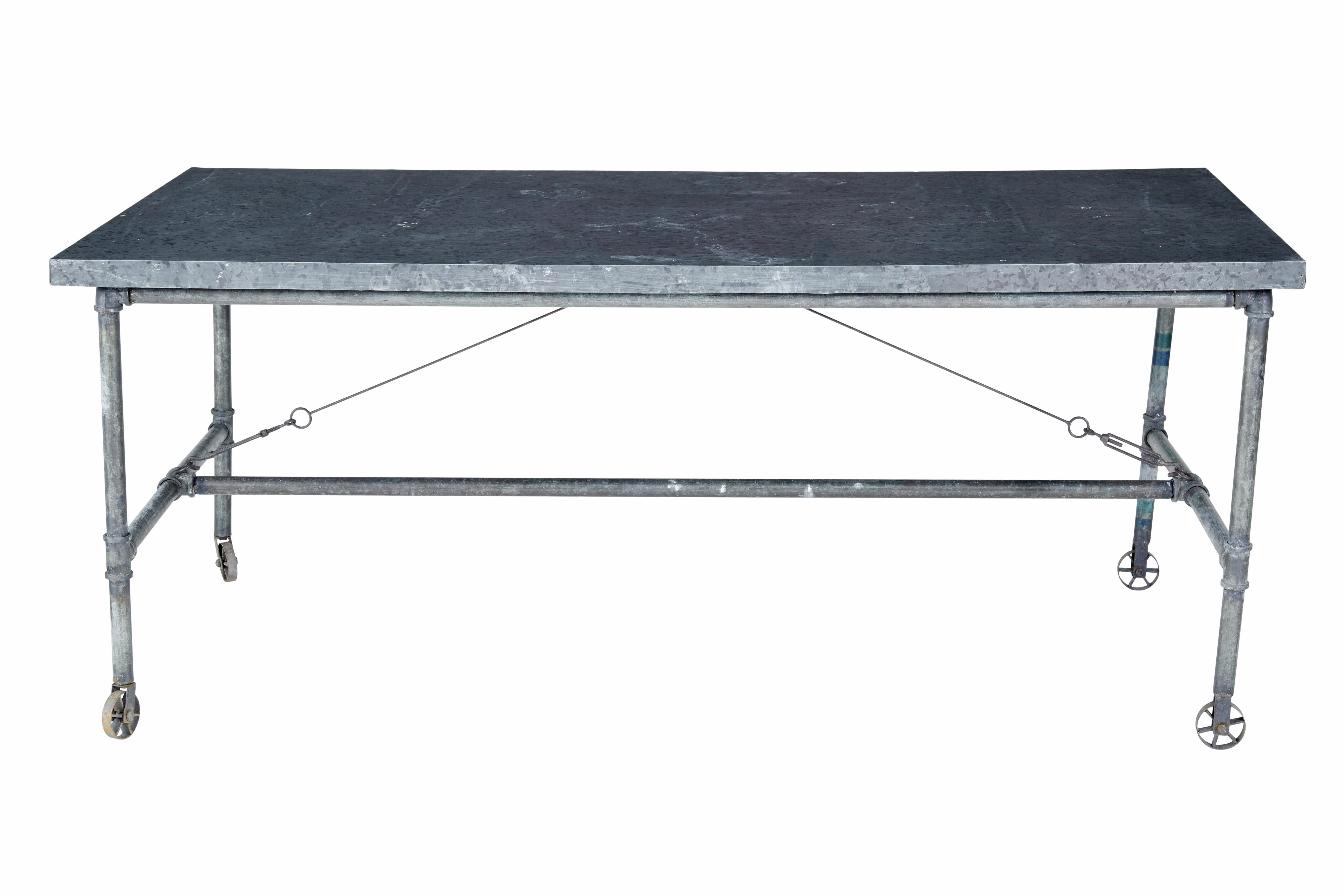 Industrieller Tisch aus recyceltem Metall aus dem frühen 20. Jahrhundert, um 1930.

Industriell gefertigter Arbeitstisch aus einem Rohrrahmen, der von Bahren getragen wird.  Ausgestattet mit festen Rädern an einem Ende und drehbaren Rädern am