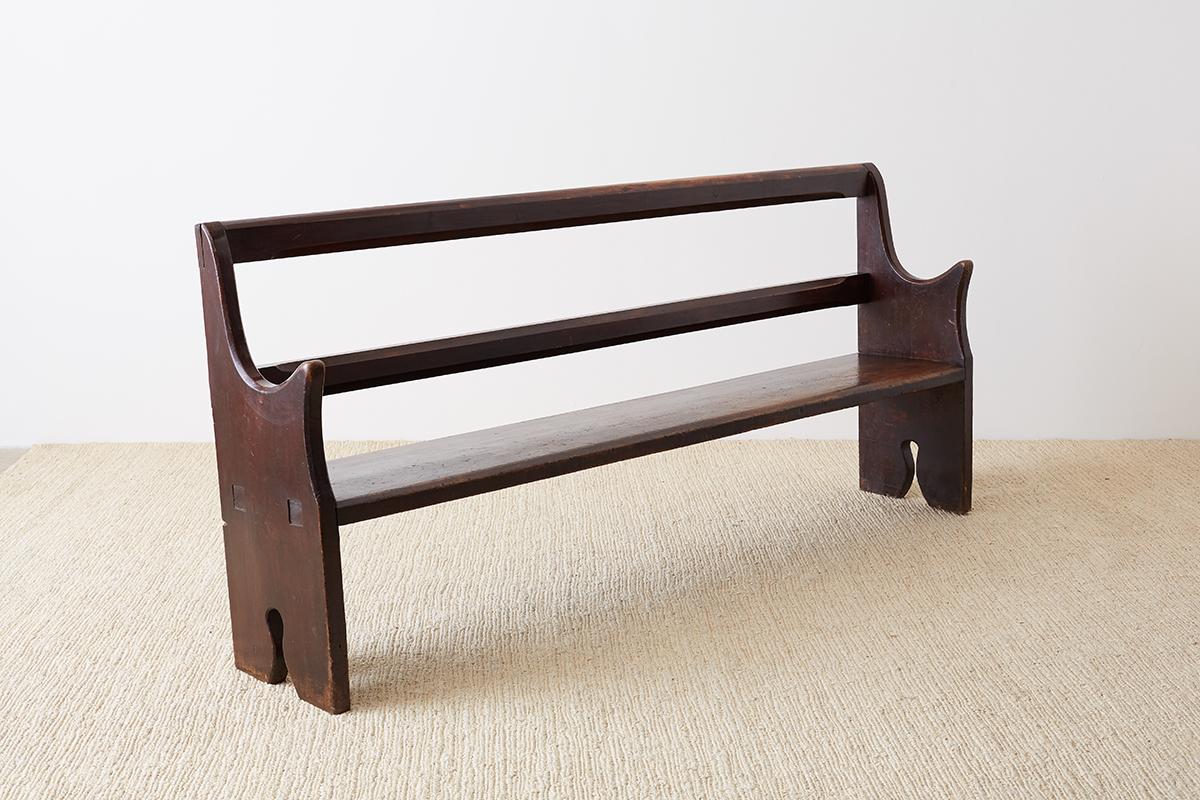 Interesting early 20th century church pew or bench constructed from redwood. Made in a minimalist style with a open back and a flat bench seat. The ends have curved arms and shaped legs. Good joinery with a mortise and tenon craftsmanship and dove